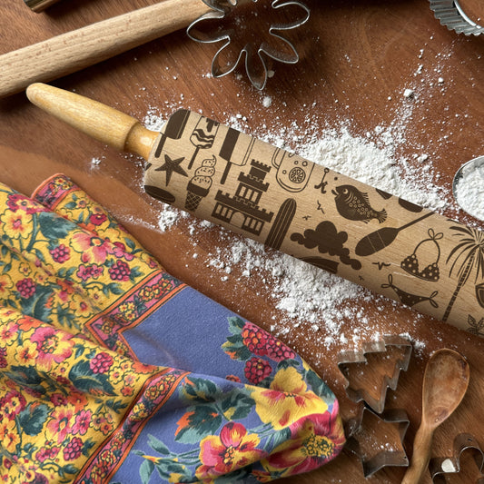 Decorative rolling pin with embossed designs on a wooden surface with flour and baking tools.