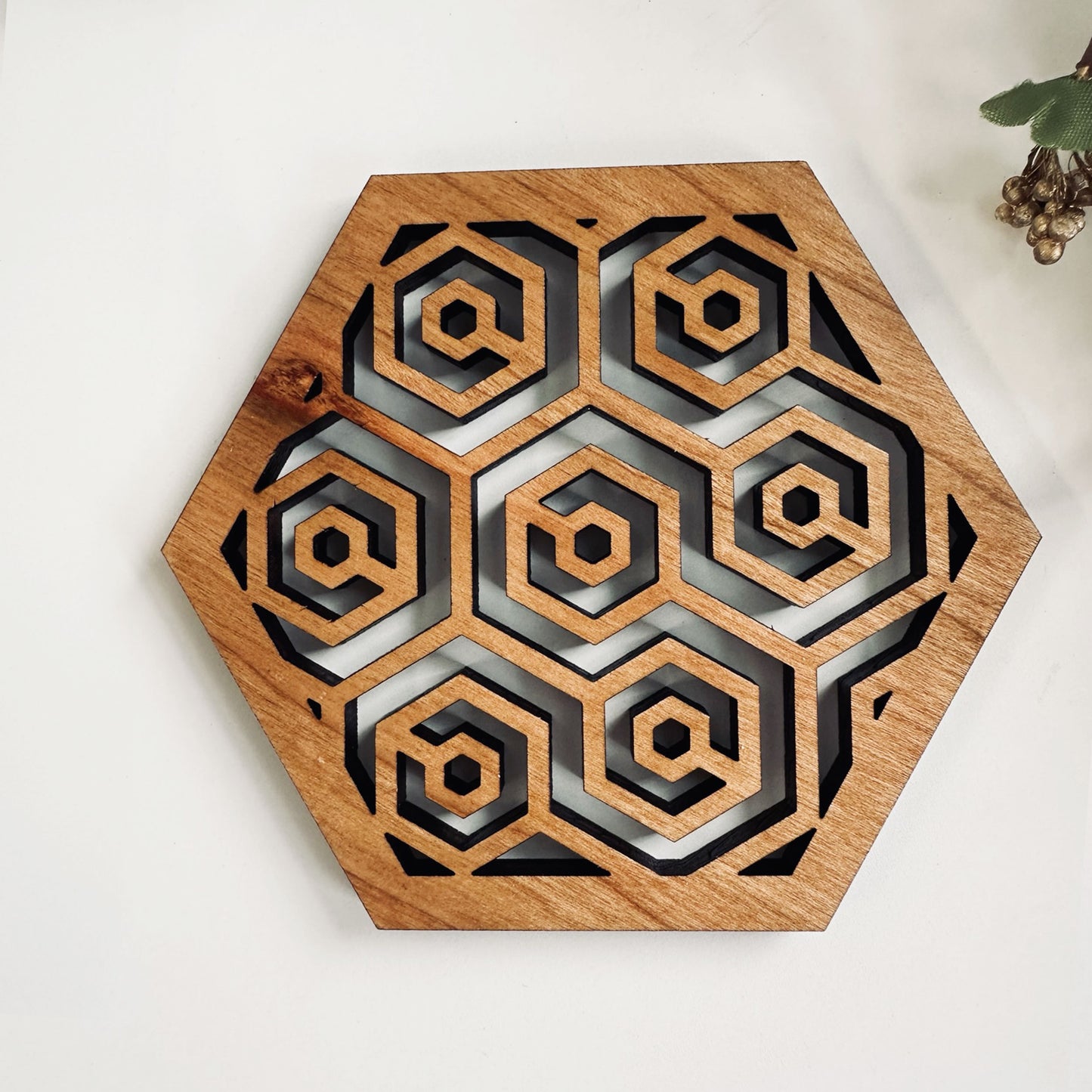 A wooden laser-cut hexagonal coaster with a honeycomb design on on a white background.