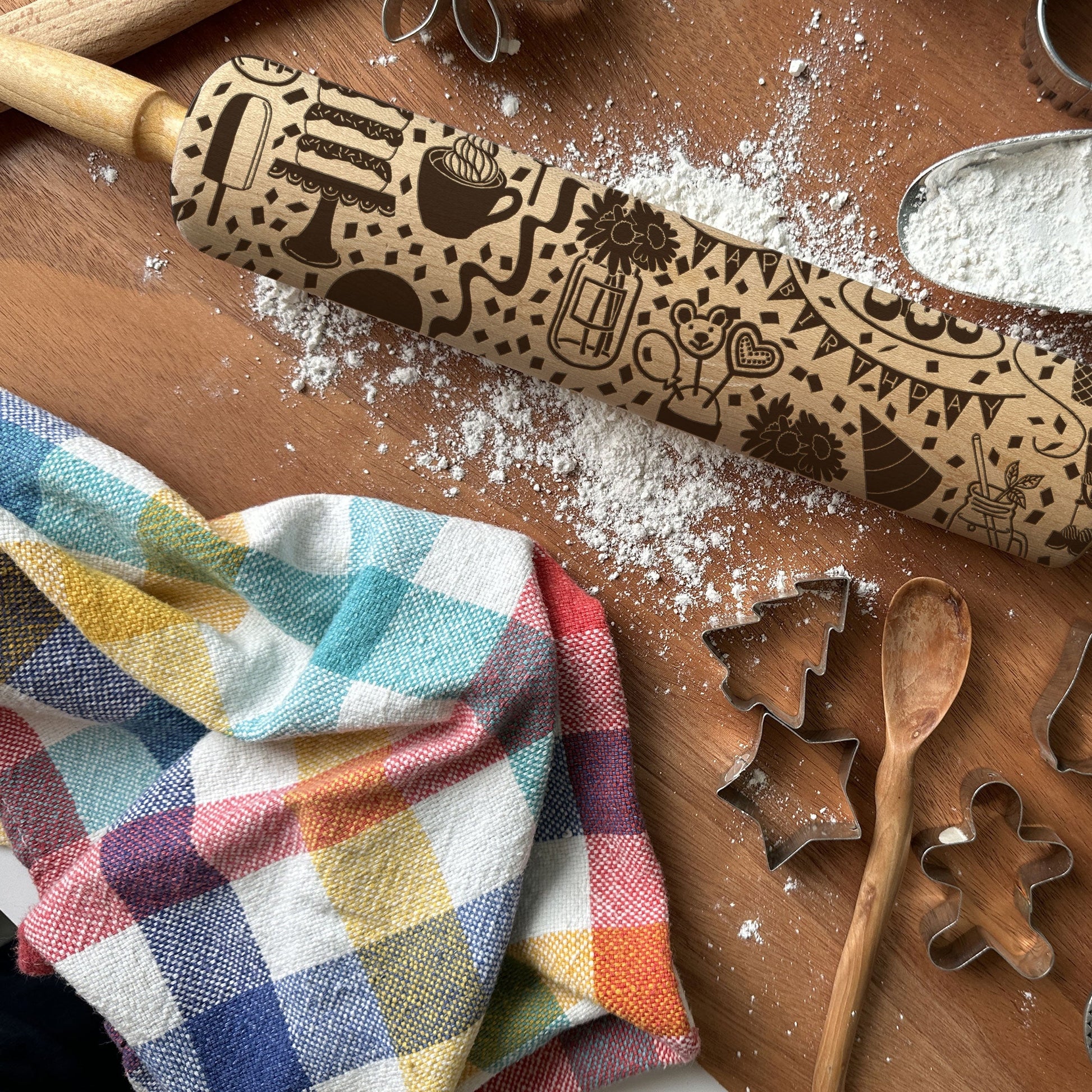 Decorative rolling pin with embossed designs on a wooden surface with flour and baking tools.