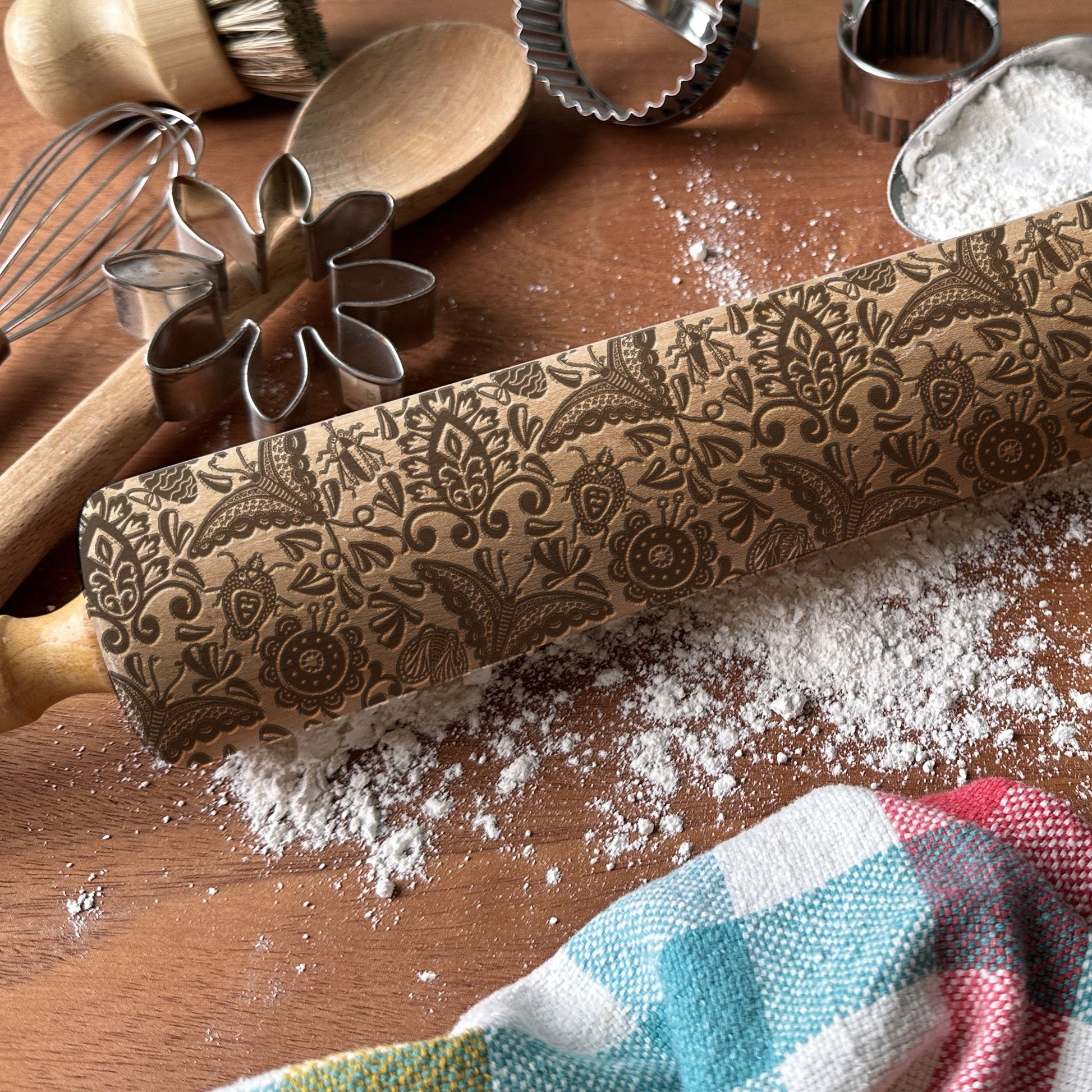 Decorative embossed rolling pin on a wooden surface with flour and kitchen tools.