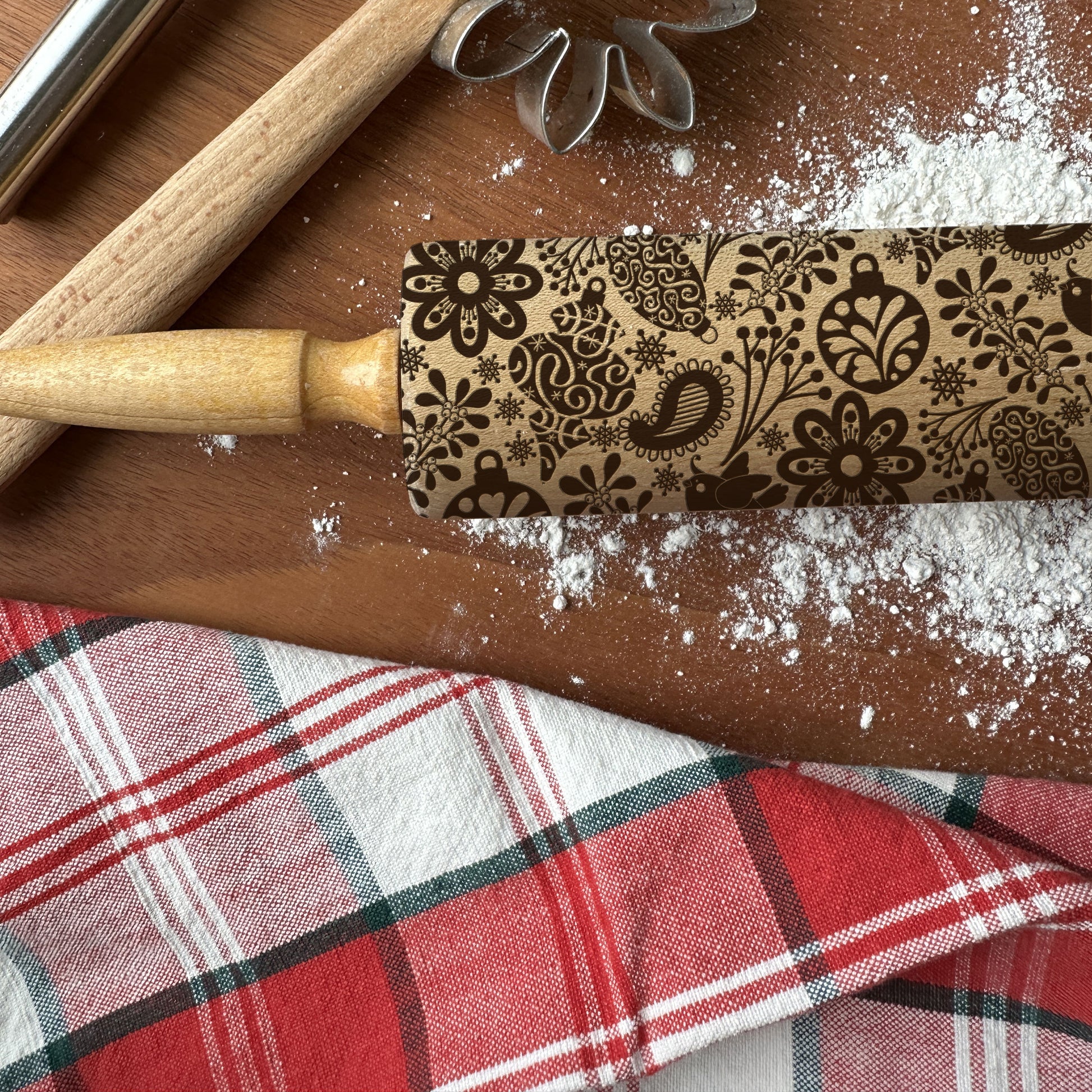 Decorative rolling pin with floral patterns on a wooden surface with flour and a plaid cloth.