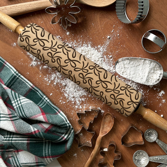 Wooden rolling pin with embossed pattern on a wooden surface with baking tools and flour.