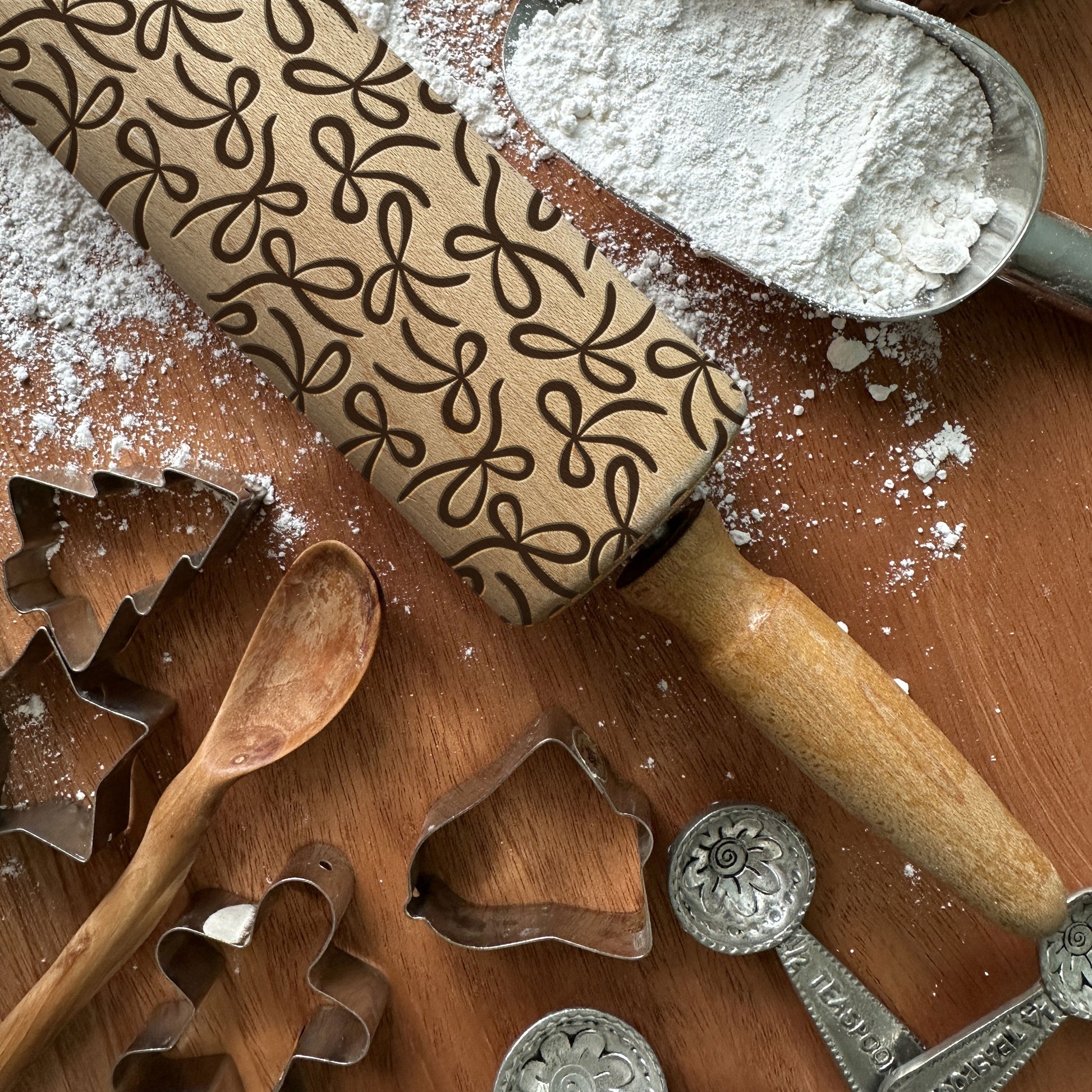 Baking tools including a rolling pin with a pattern, cookie cutters, and a wooden spoon on a wooden surface.