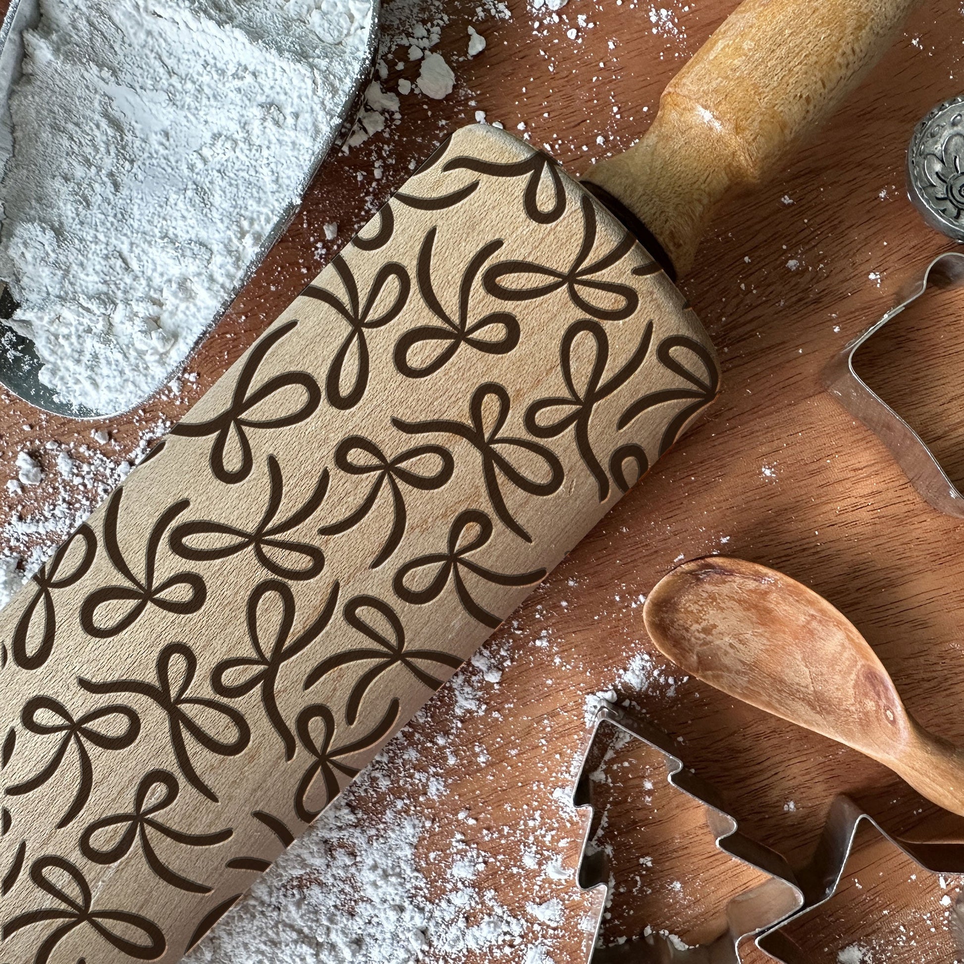 Wooden rolling pin with decorative patterns on a wooden surface with cookie cutters and flour.