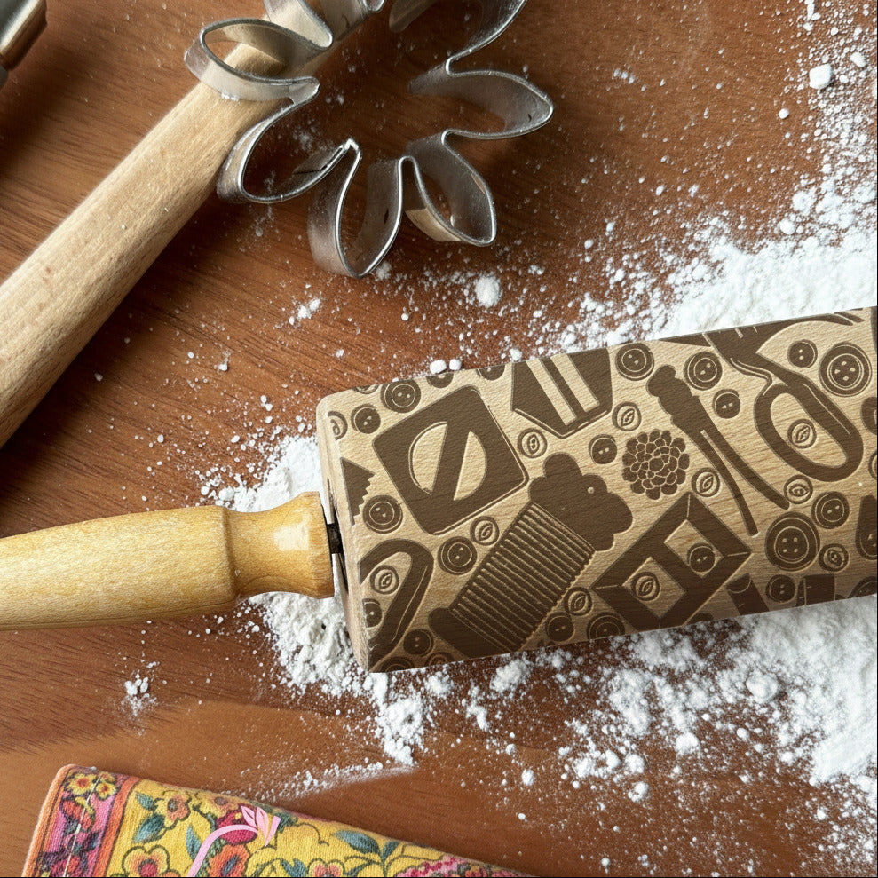 Decorative rolling pin with floral design on a wooden surface with flour, next to a traditional rolling pin and cookie cutters.