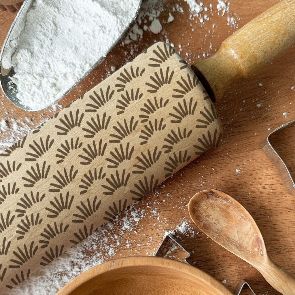 Rolling pin with pattern, cookie cutters, and wooden spoon on a wooden surface with flour, branded 'Pickle and Peach Studio'.