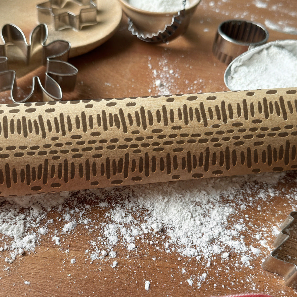 Wooden rolling pin with embossed pattern on a wooden surface with flour, branded 'Pickle and Peach Studio'.