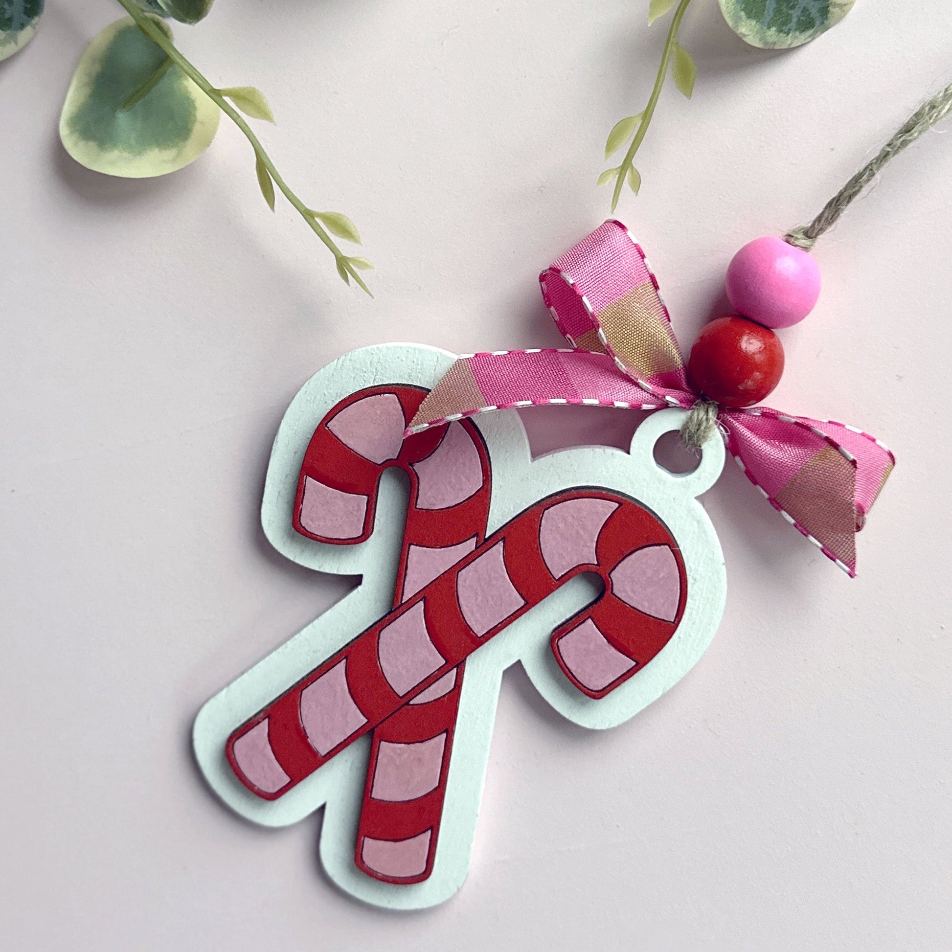 Pink candy cane ornament with a bow on a textured background with greenery.