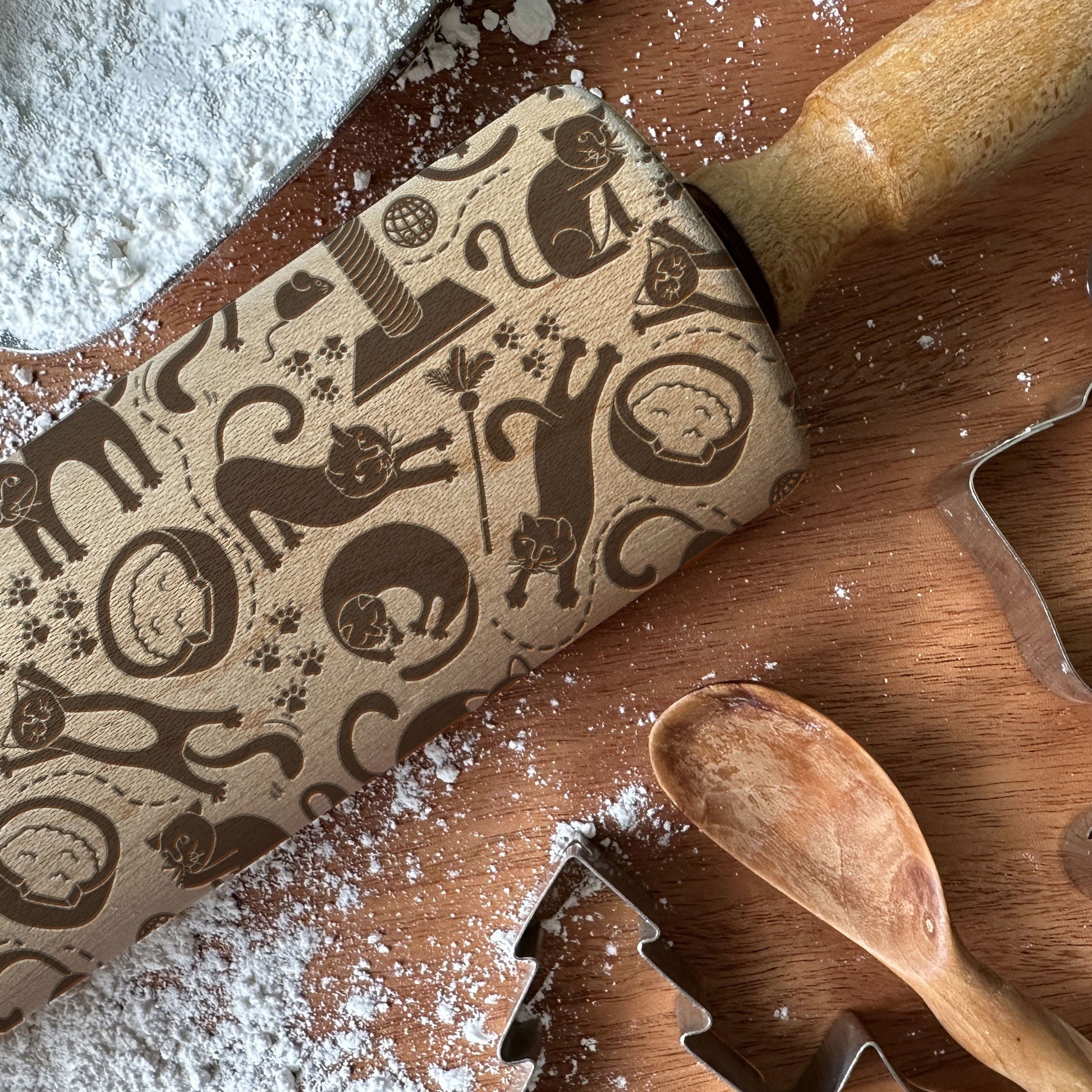 Baking tools including a rolling pin, wooden spoon, and cookie cutters on a surface with flour.
