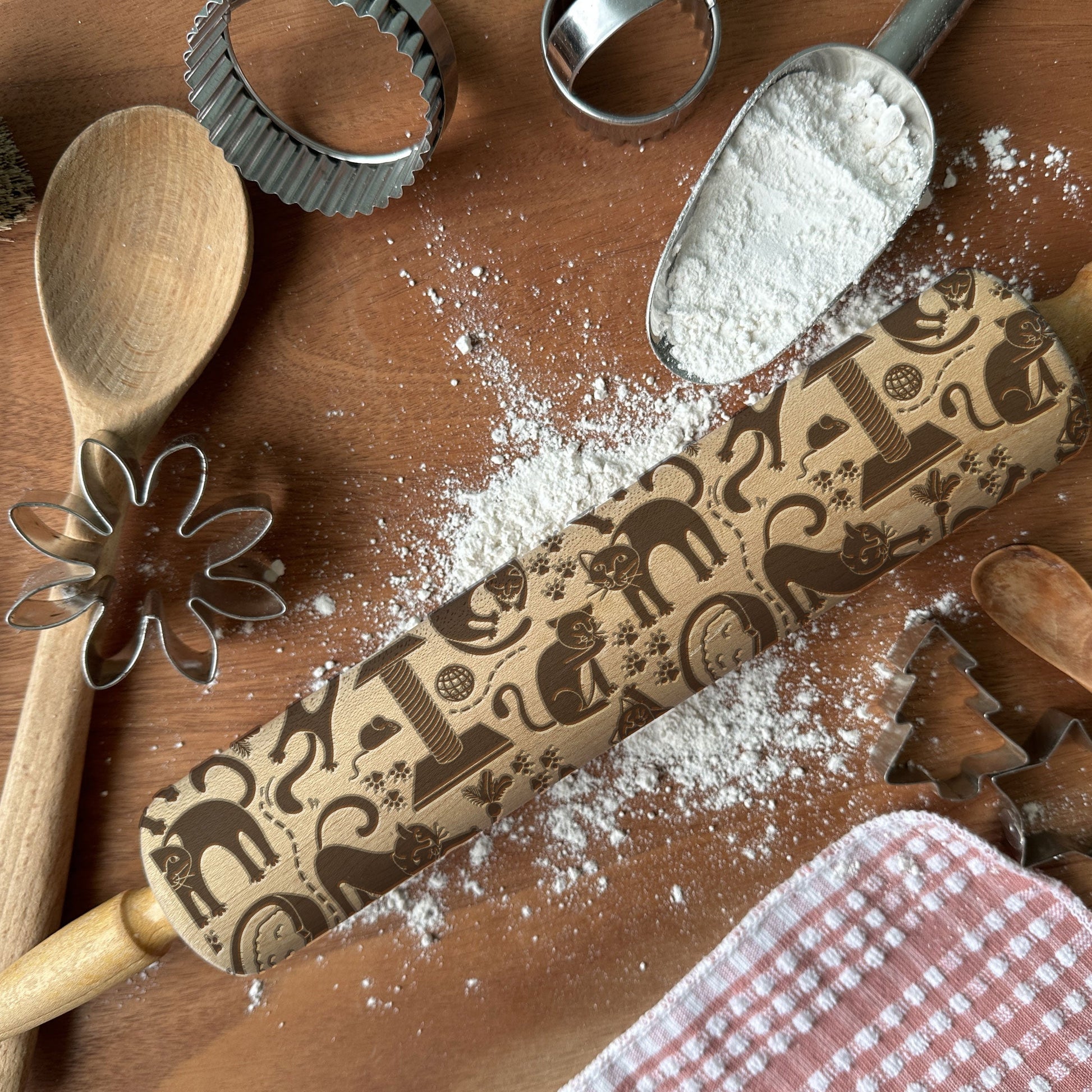 Decorative rolling pin with embossed designs on a wooden surface with flour and baking tools.
