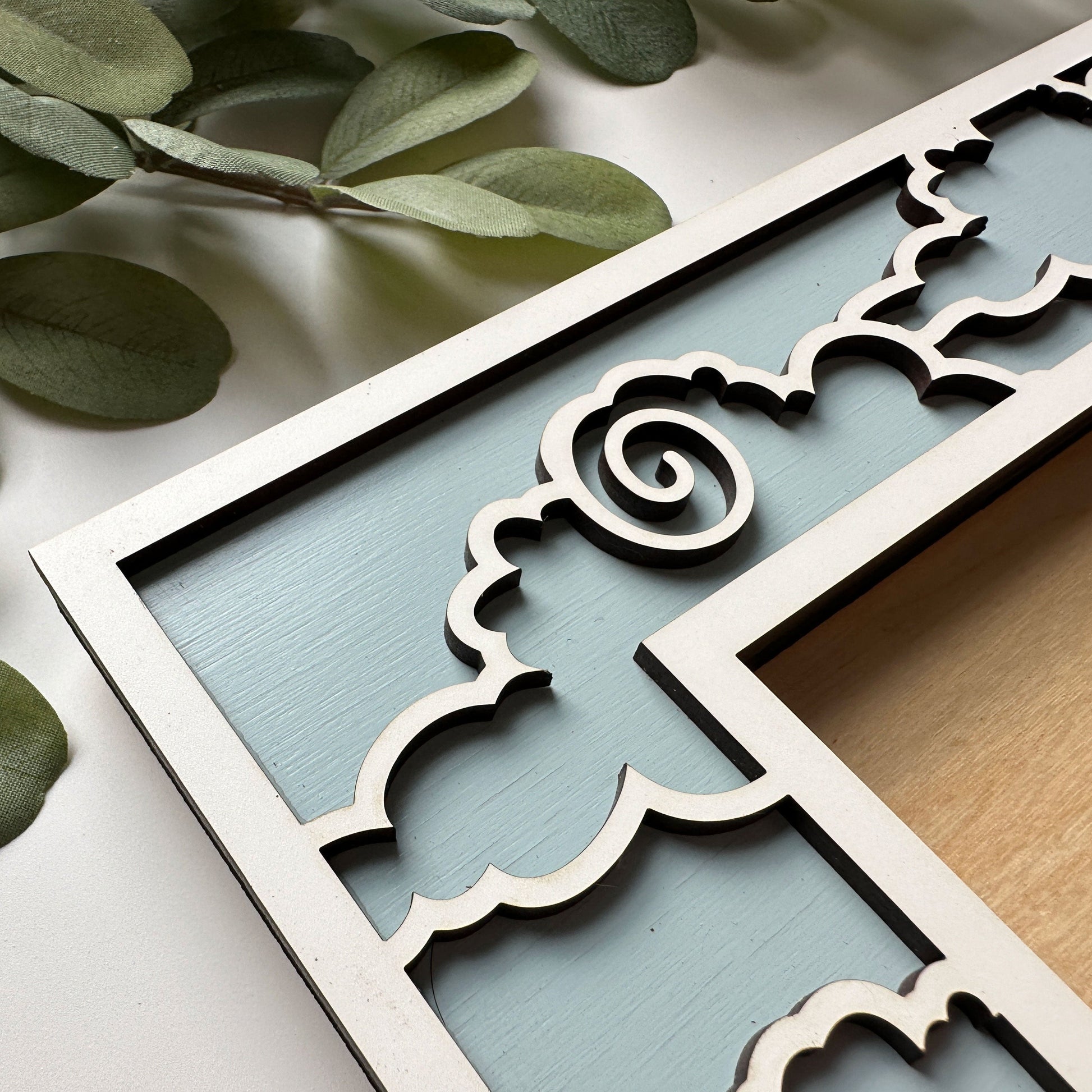 Decorative picture frame with intricate cut-out design on a light background with green leaves.