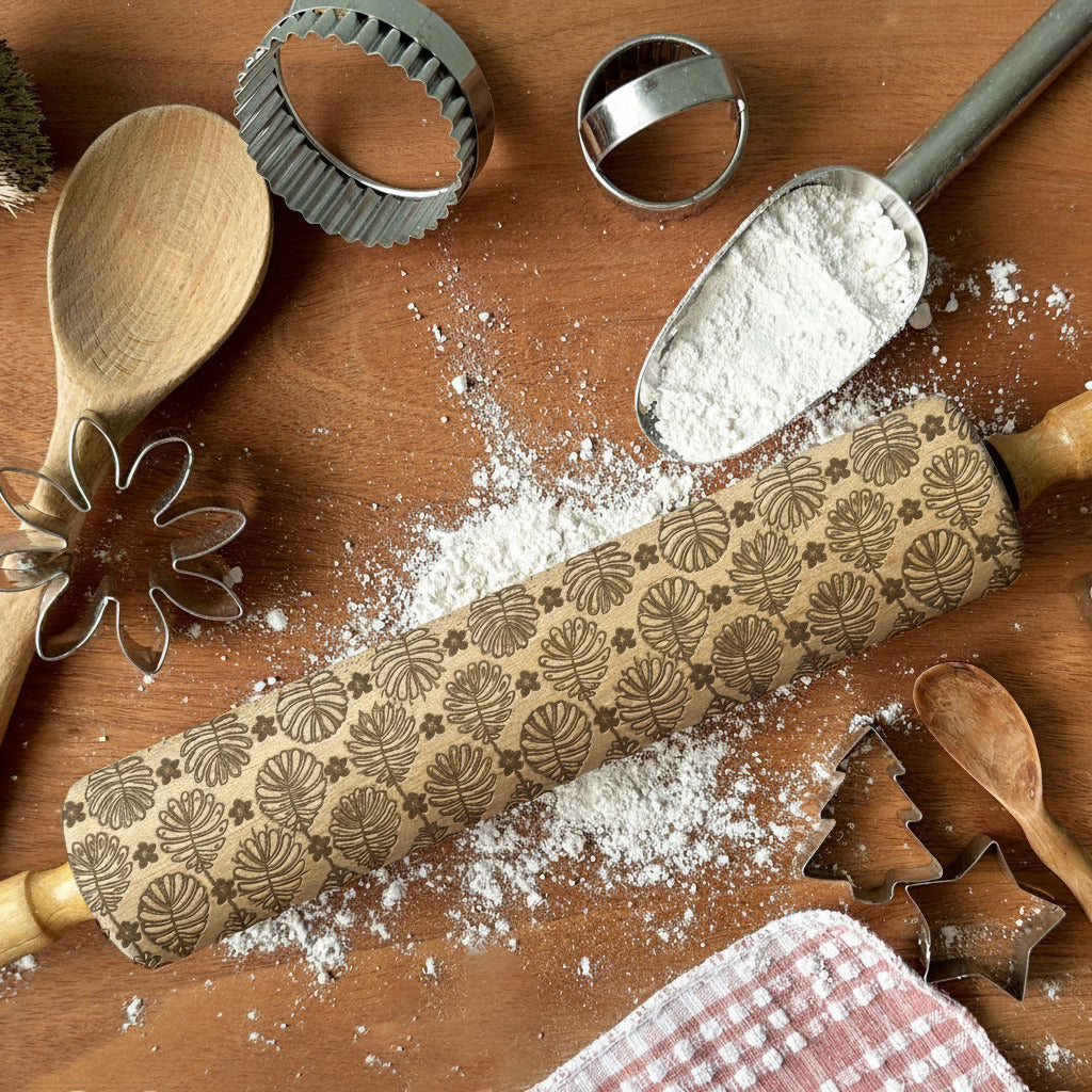 Decorative rolling pin with embossed patterns on a wooden surface with flour and baking tools.