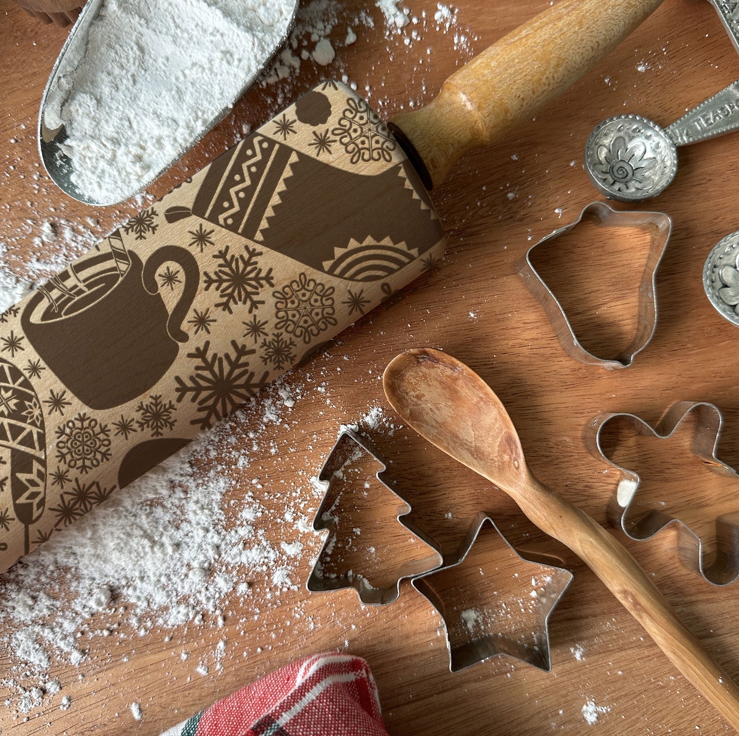 Baking tools including a rolling pin, cookie cutters, and measuring spoons on a wooden surface with flour.