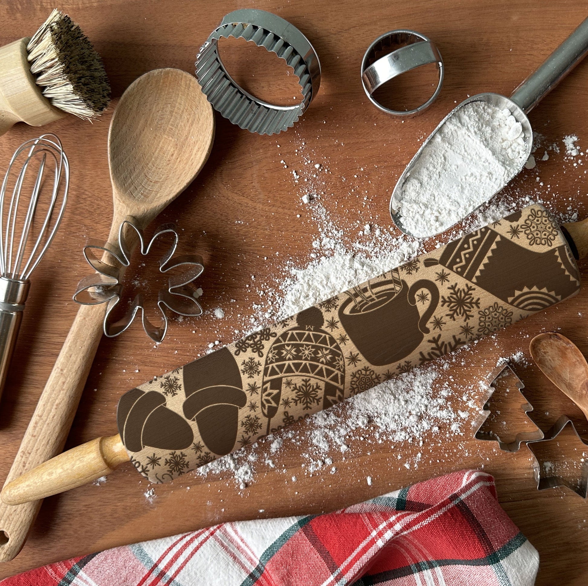 Baking tools including a rolling pin with a coffee-themed design, wooden spoon, whisk, and cookie cutters on a wooden surface.