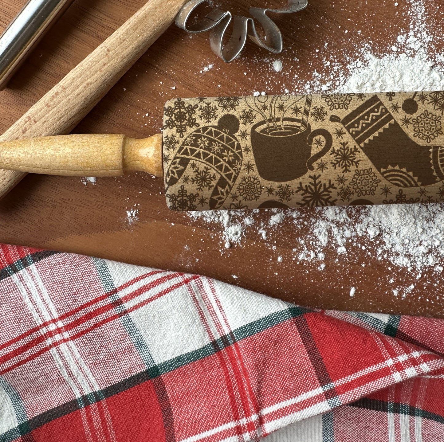 Decorative rolling pin with a pattern on a wooden surface with flour and a plaid cloth.