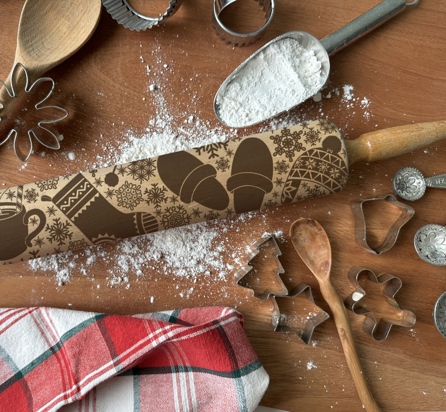 Baking tools including a rolling pin with embossed designs, cookie cutters, and flour on a wooden surface.
