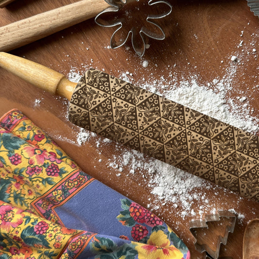Decorative embossed rolling pin on a wooden surface with flour and baking tools.