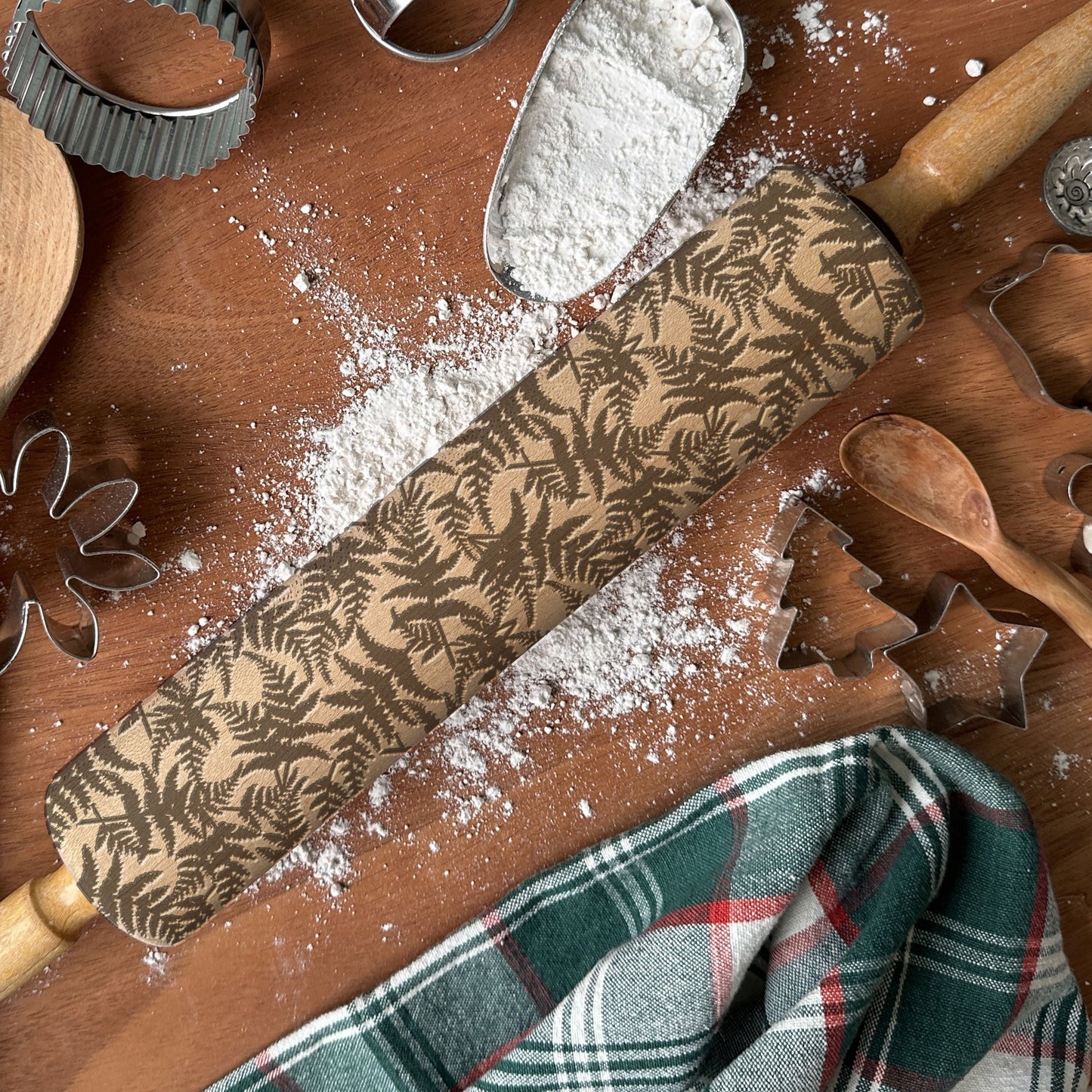 Wooden rolling pin with leaf pattern on a wooden surface with flour and baking tools.