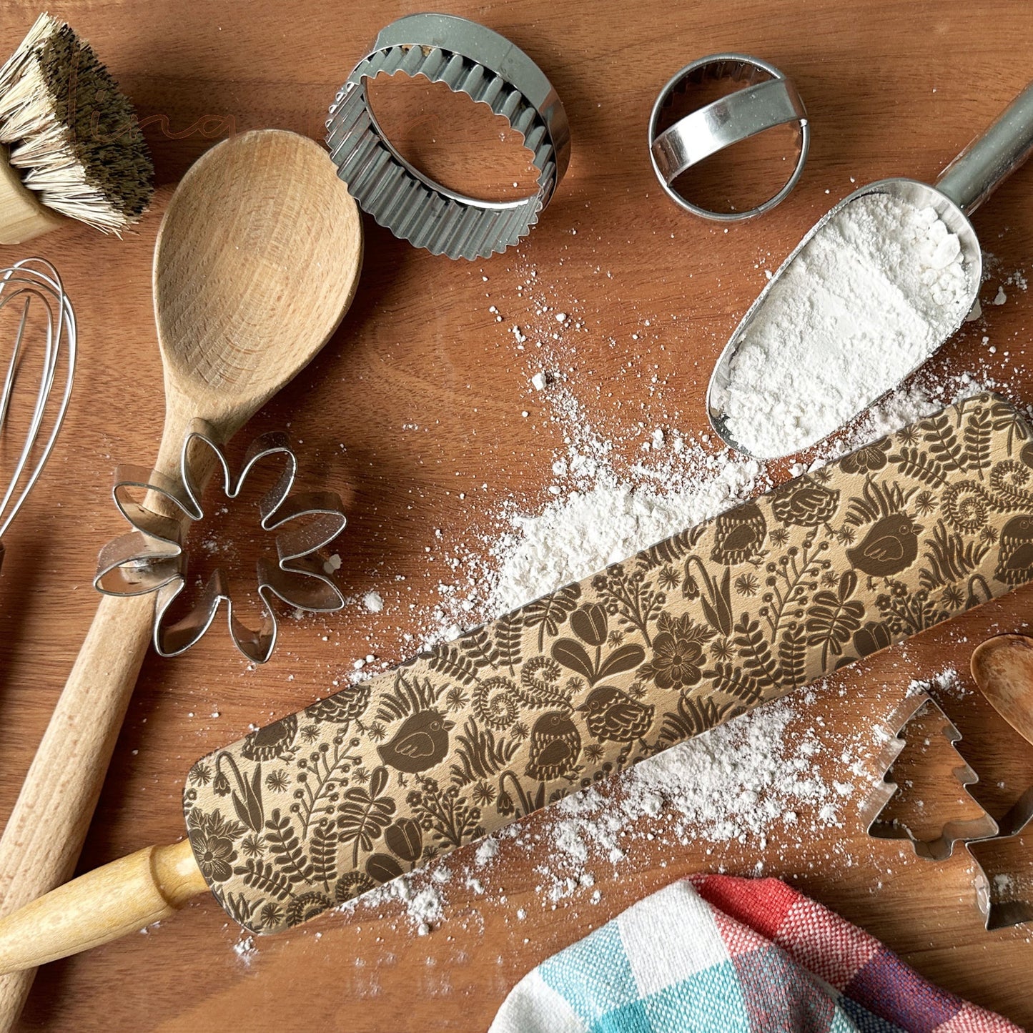 Wooden rolling pin with floral patterns on a wooden surface with baking tools and flour.