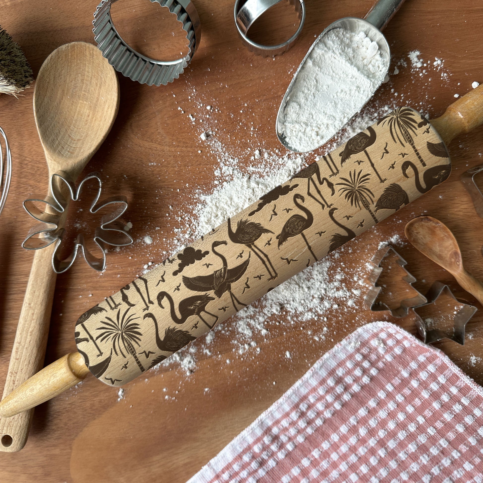 Wooden rolling pin with embossed designs on a wooden surface with flour and baking tools.
