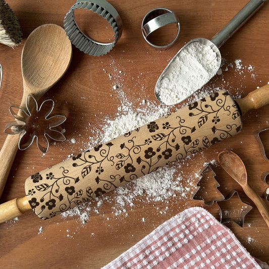 Decorative rolling pin with floral patterns on a wooden surface with baking tools and flour.