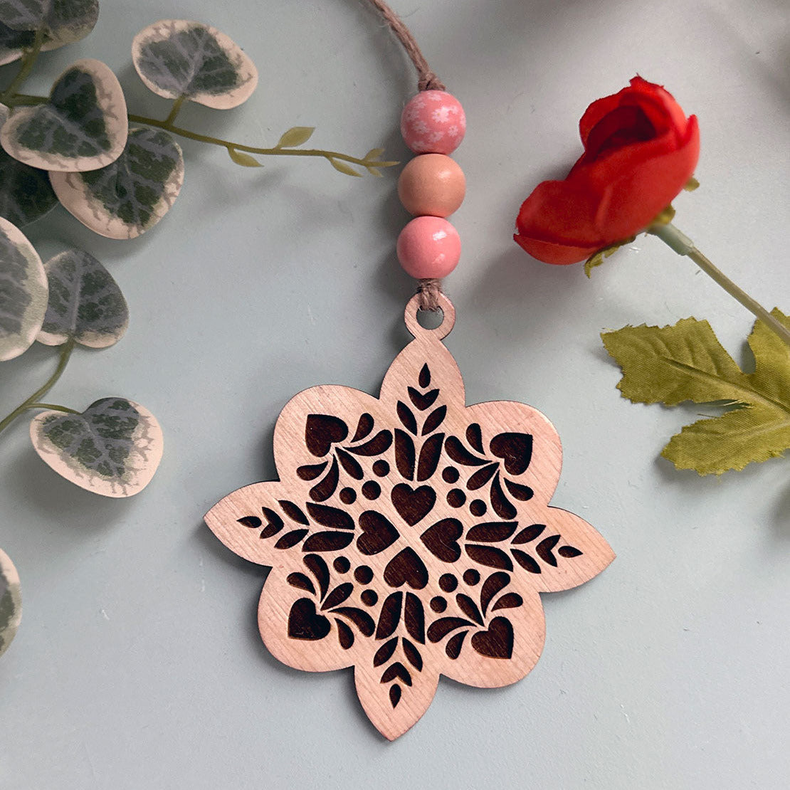 Decorative pink flower-shaped pendant with intricate cut-out design on a light gray background with floral elements.