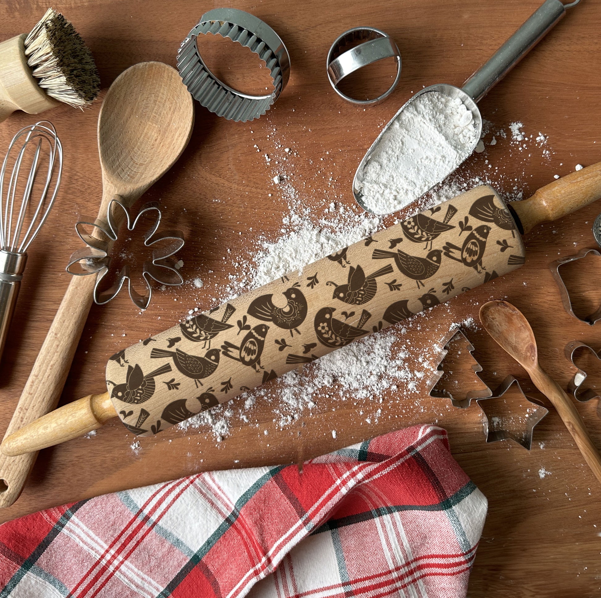 Wooden rolling pin with embossed designs on a wooden surface with baking tools.