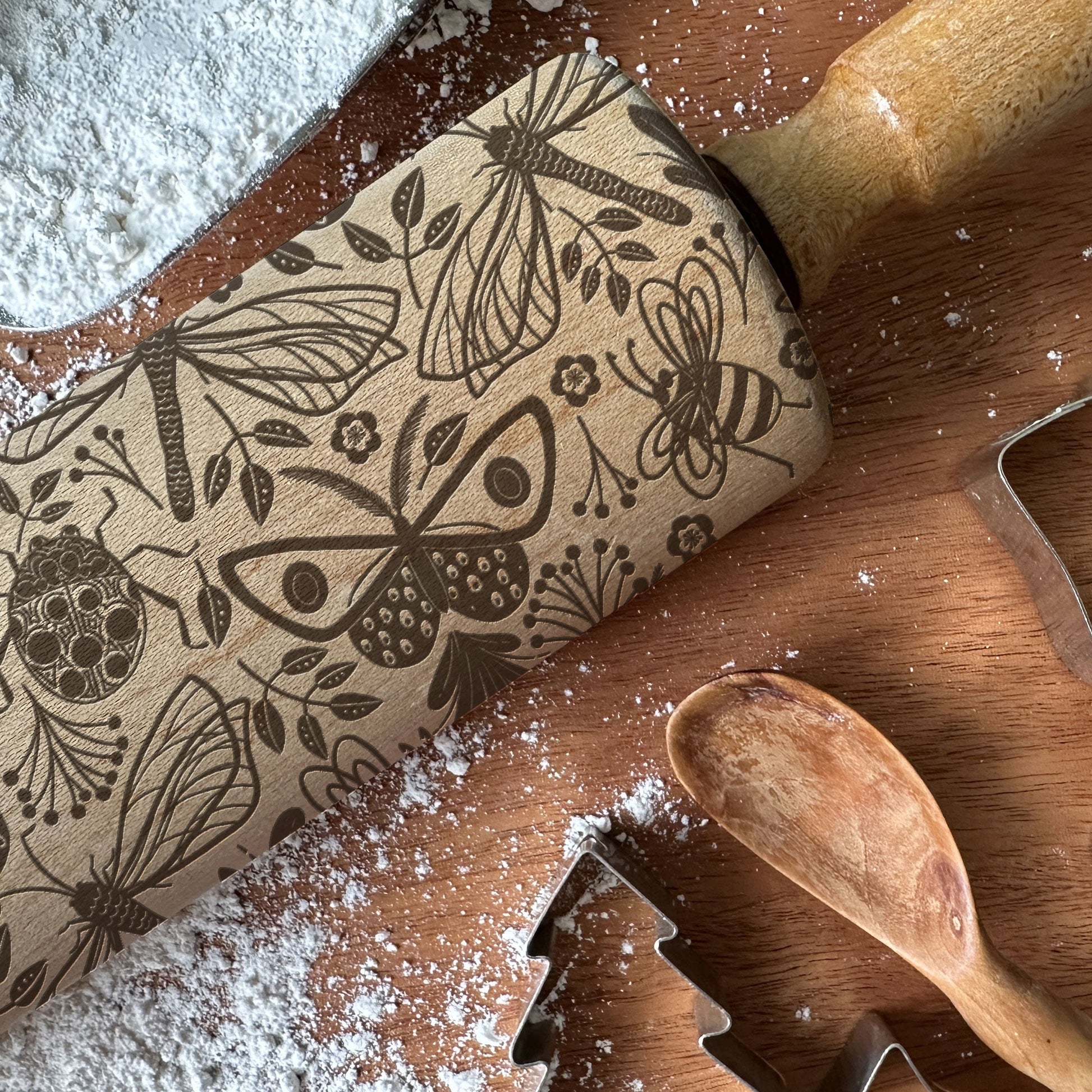 Wooden rolling pin with embossed designs on a wooden surface with flour and cookie cutters.