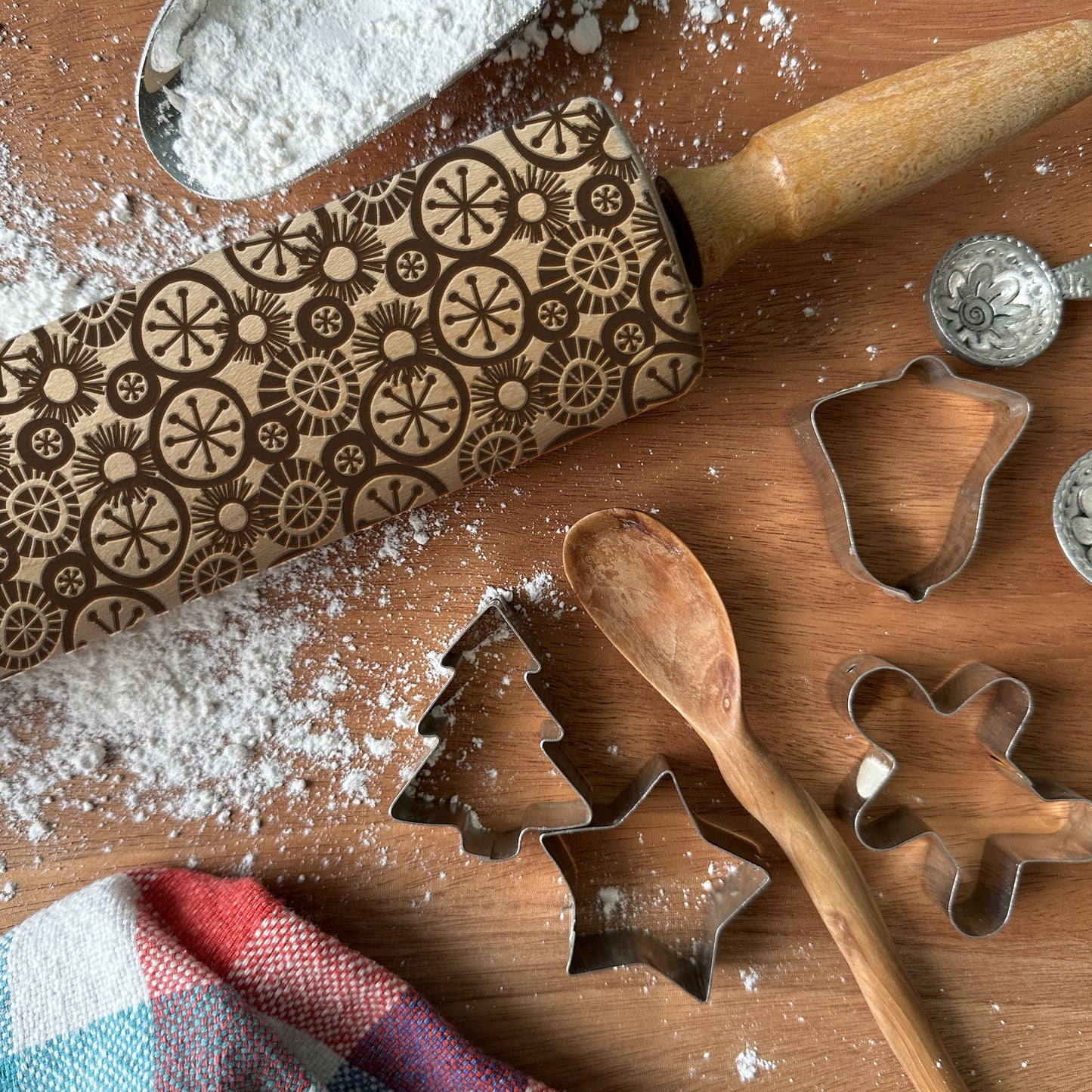 Baking tools including a rolling pin, cookie cutters, and a embossed rolling pin on a wooden surface with flour.