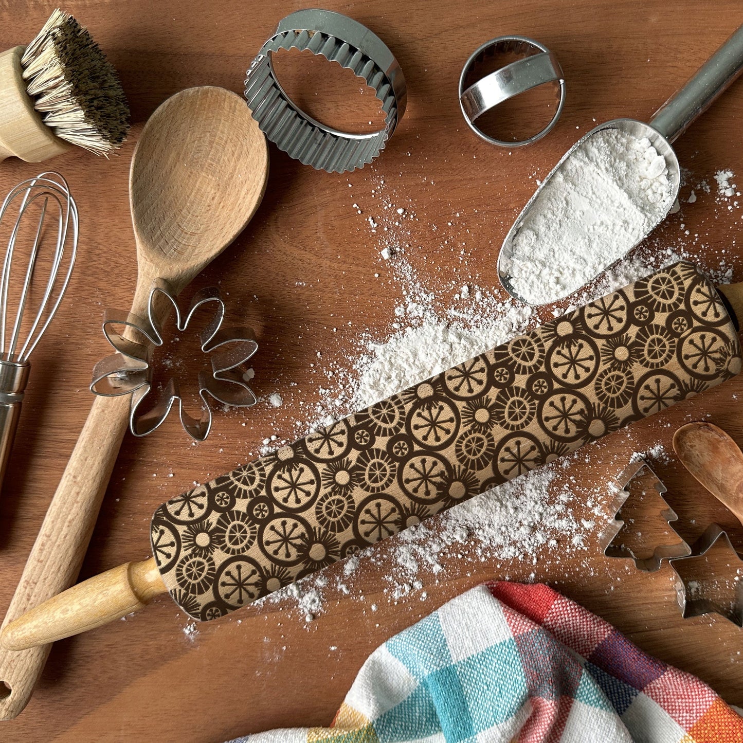 Wooden rolling pin with decorative patterns on a wooden surface with baking tools and flour.