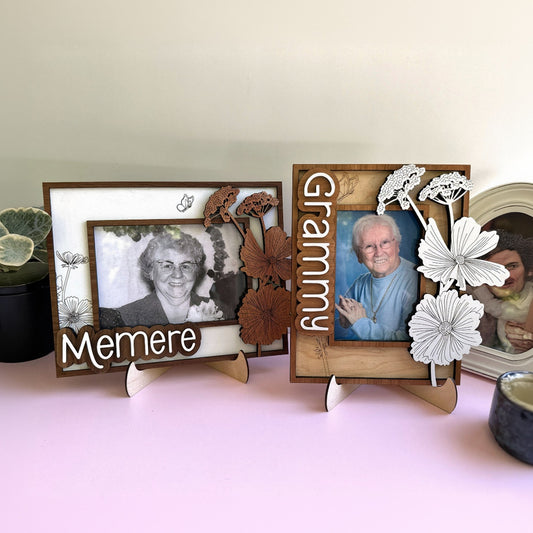 Two wooden photo frames with floral designs and cut-out flowers on a pink surface.