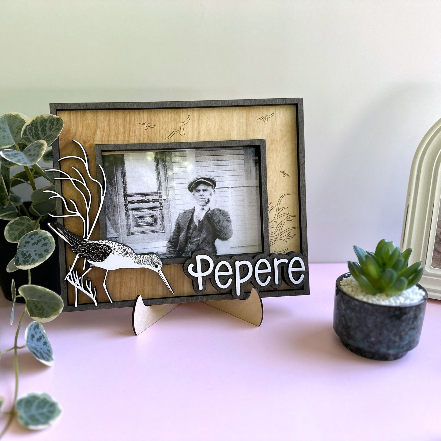 Framed photo of a man with 'Pepere' below, surrounded by plants on a table.