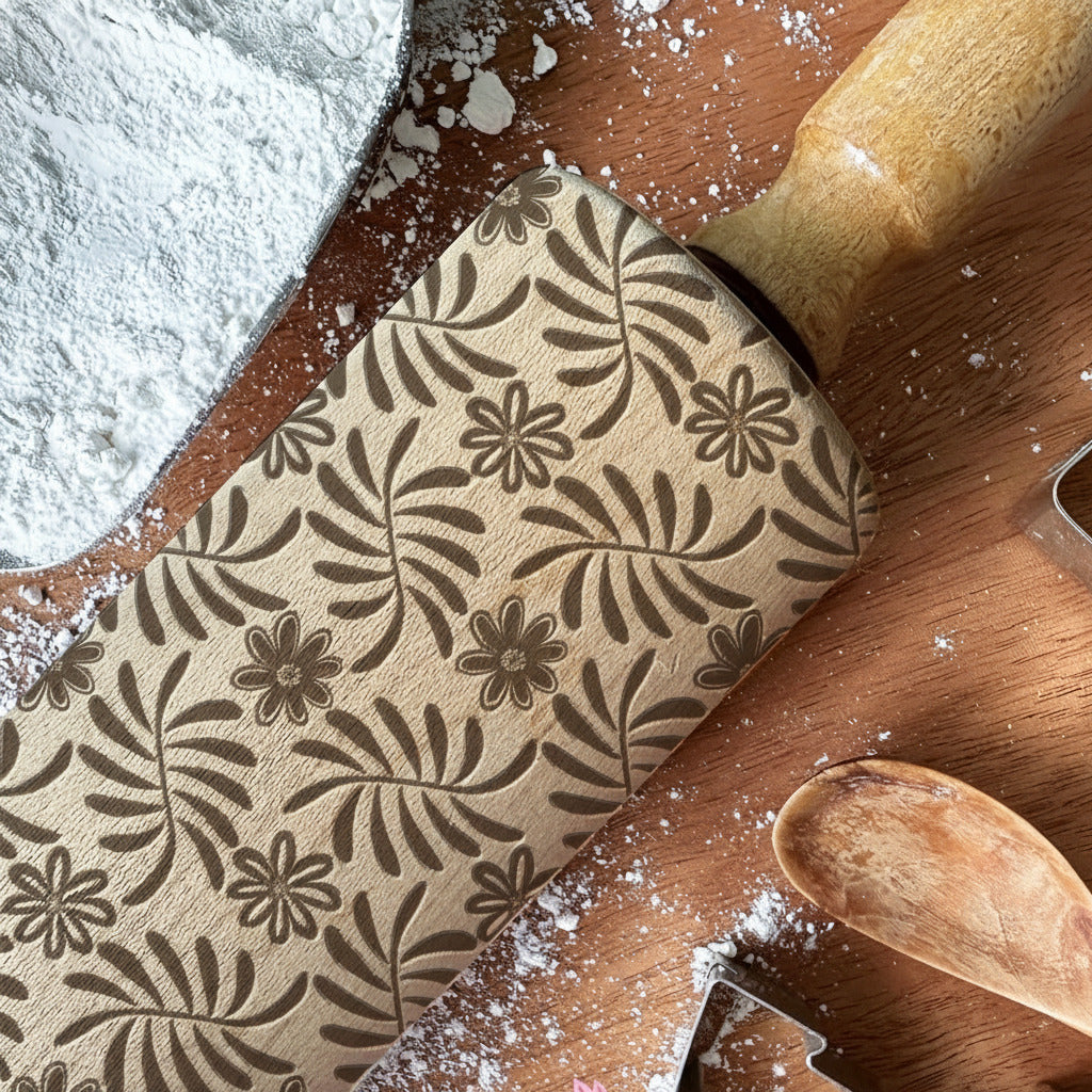 Wooden rolling pin with floral pattern and cookie cutters on a wooden surface with flour.
