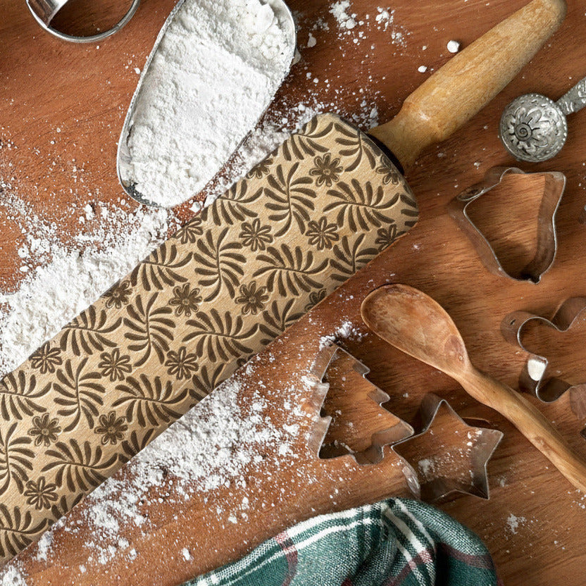 Baking tools including a rolling pin with embossed designs on a wooden surface.
