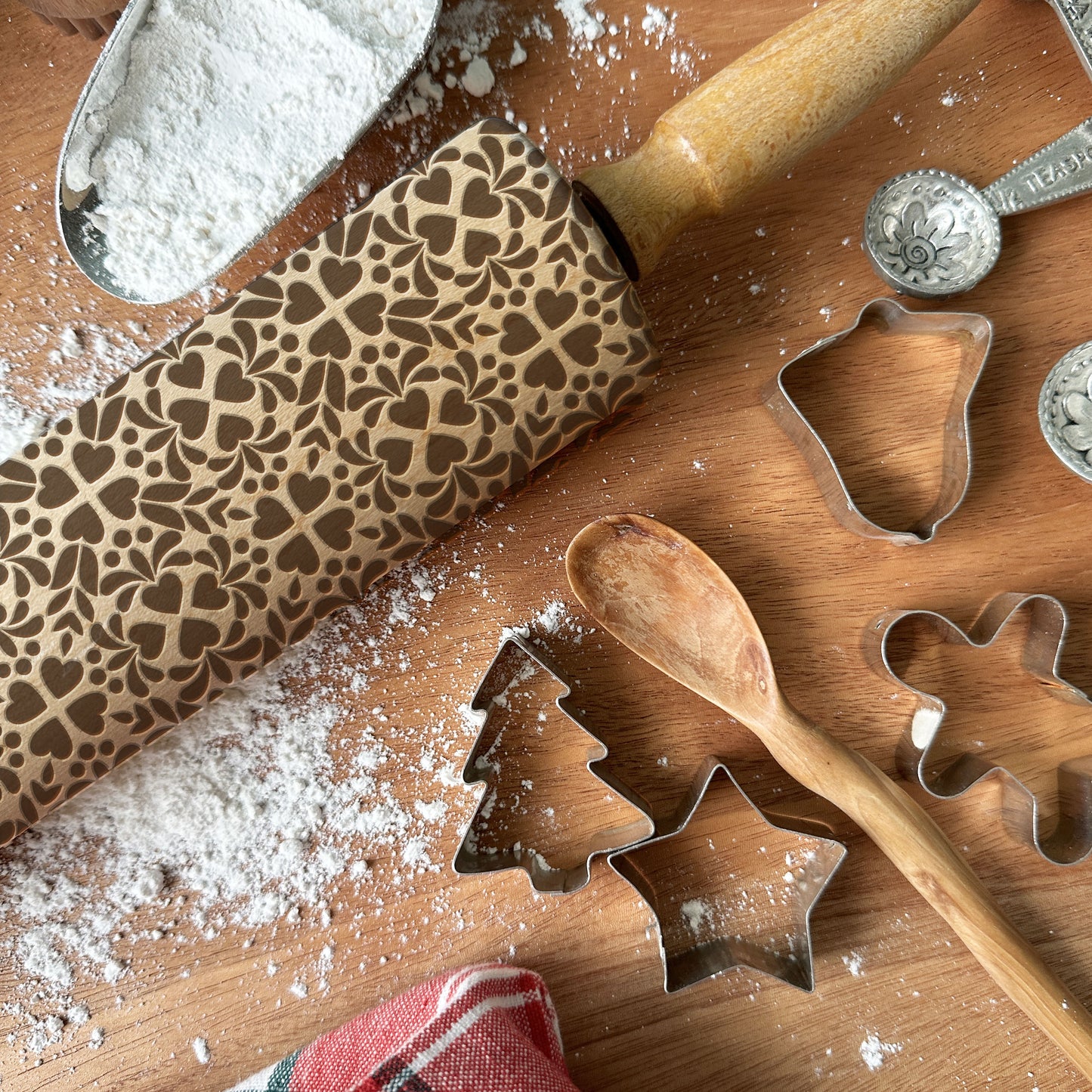 Wooden rolling pin with embossed pattern and cookie cutters on a wooden surface with flour.