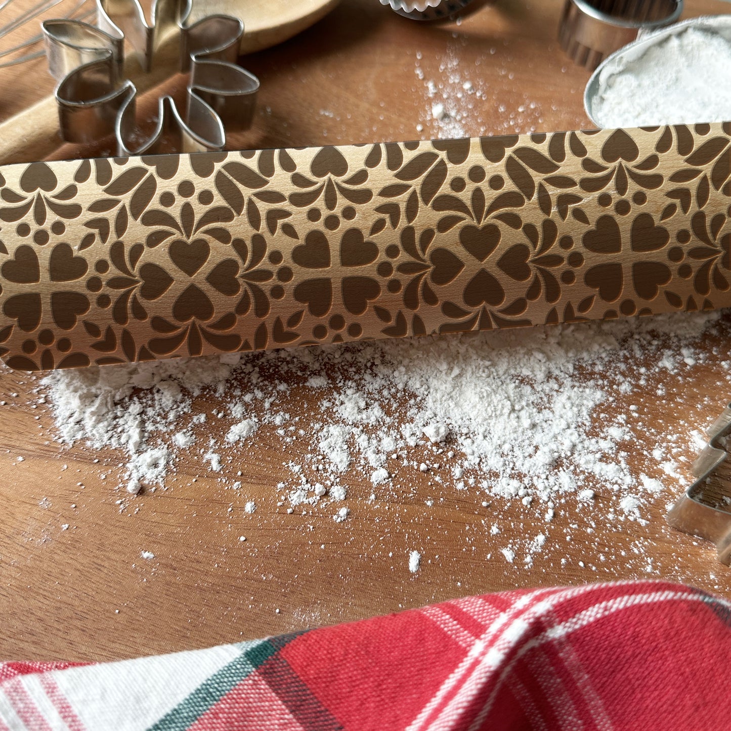 Decorative rolling pin with floral pattern on a wooden surface with flour and cookie cutters.