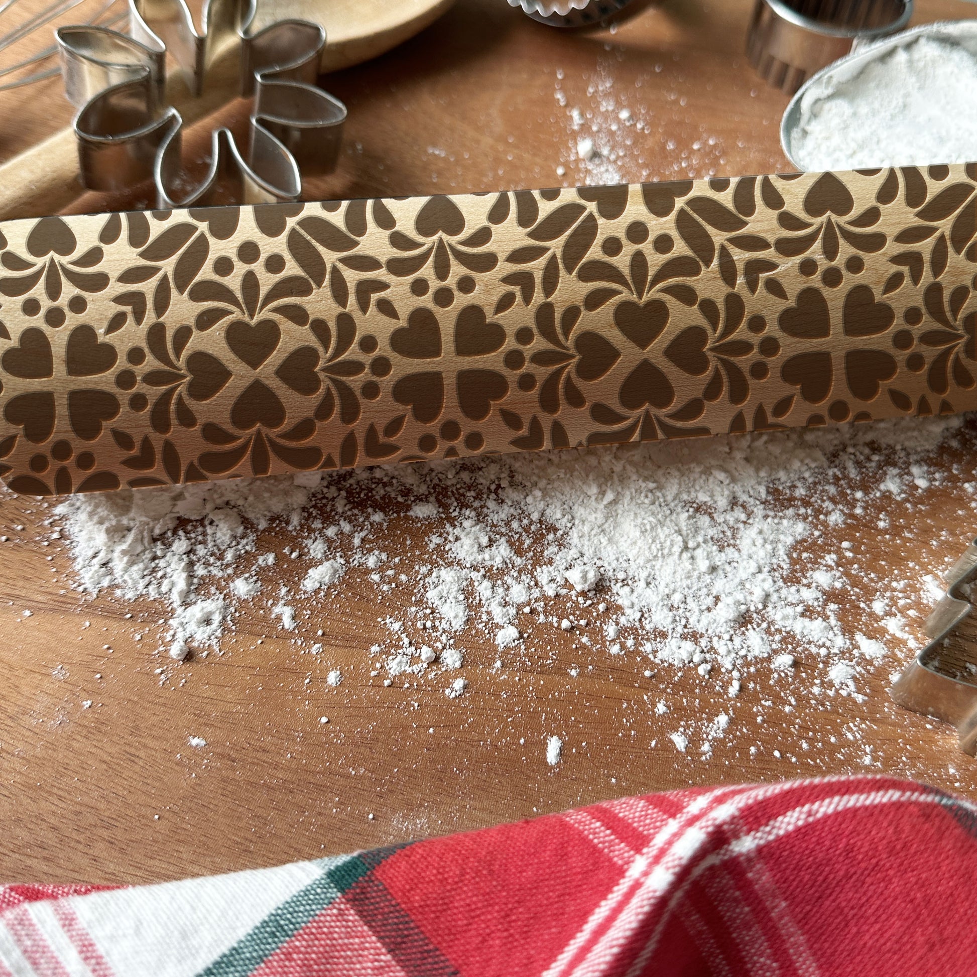 Decorative rolling pin with floral pattern on a wooden surface with flour and cookie cutters.