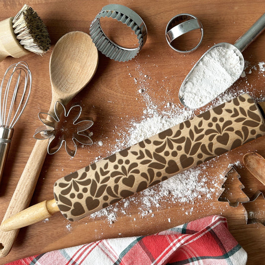 Baking tools including a rolling pin with a floral pattern on a wooden surface.