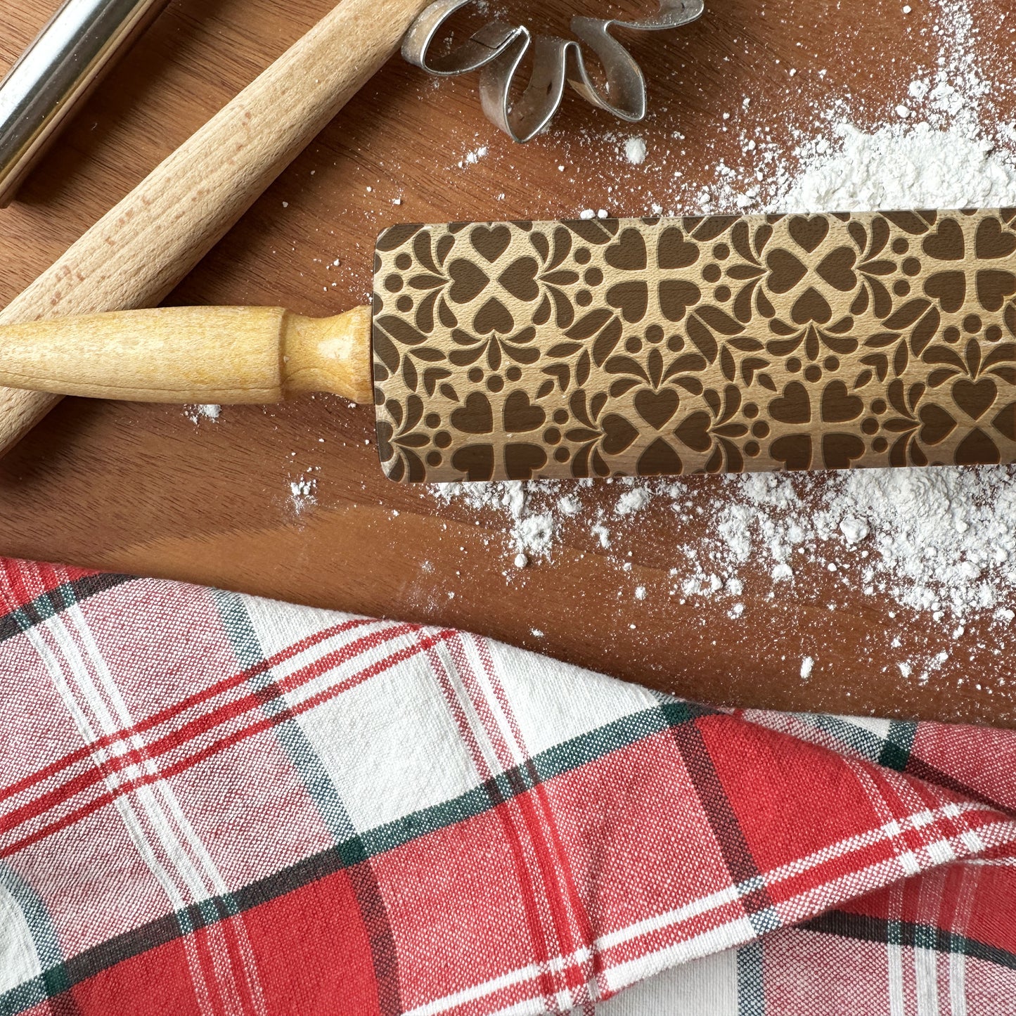 Decorative rolling pin with a pattern on a wooden surface with flour and a plaid cloth.