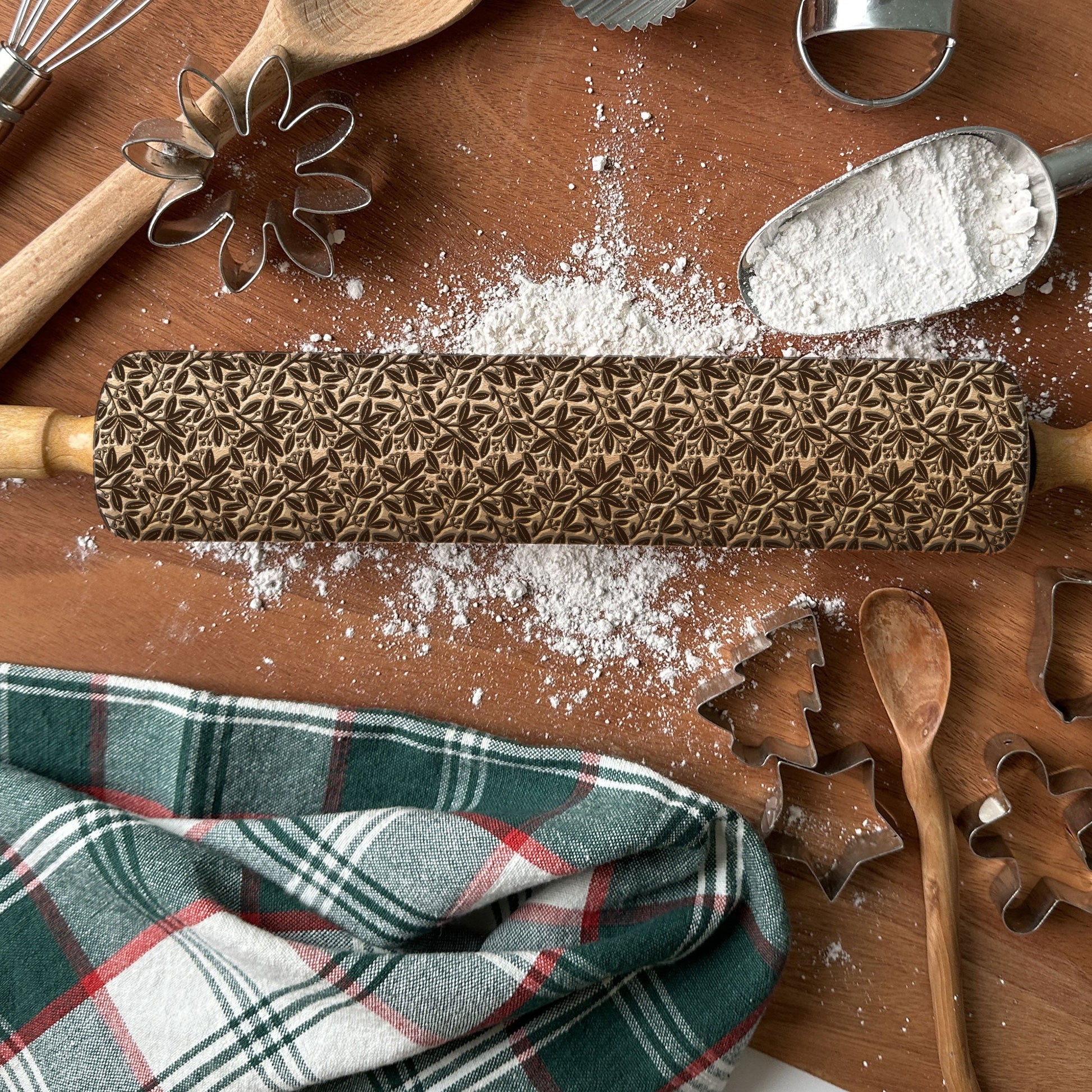 Patterned rolling pin with baking tools on a wooden surface with flour.