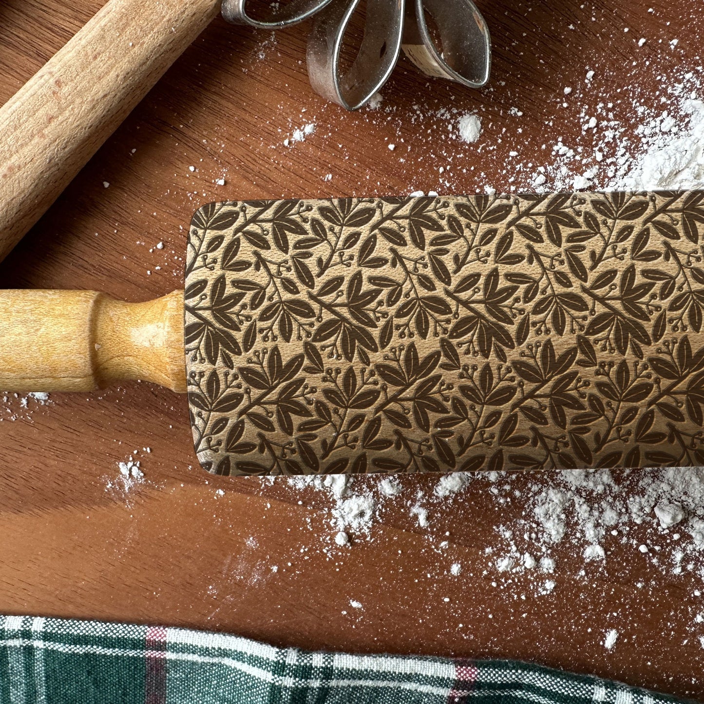 Decorative rolling pin with leaf pattern on a wooden surface with flour.