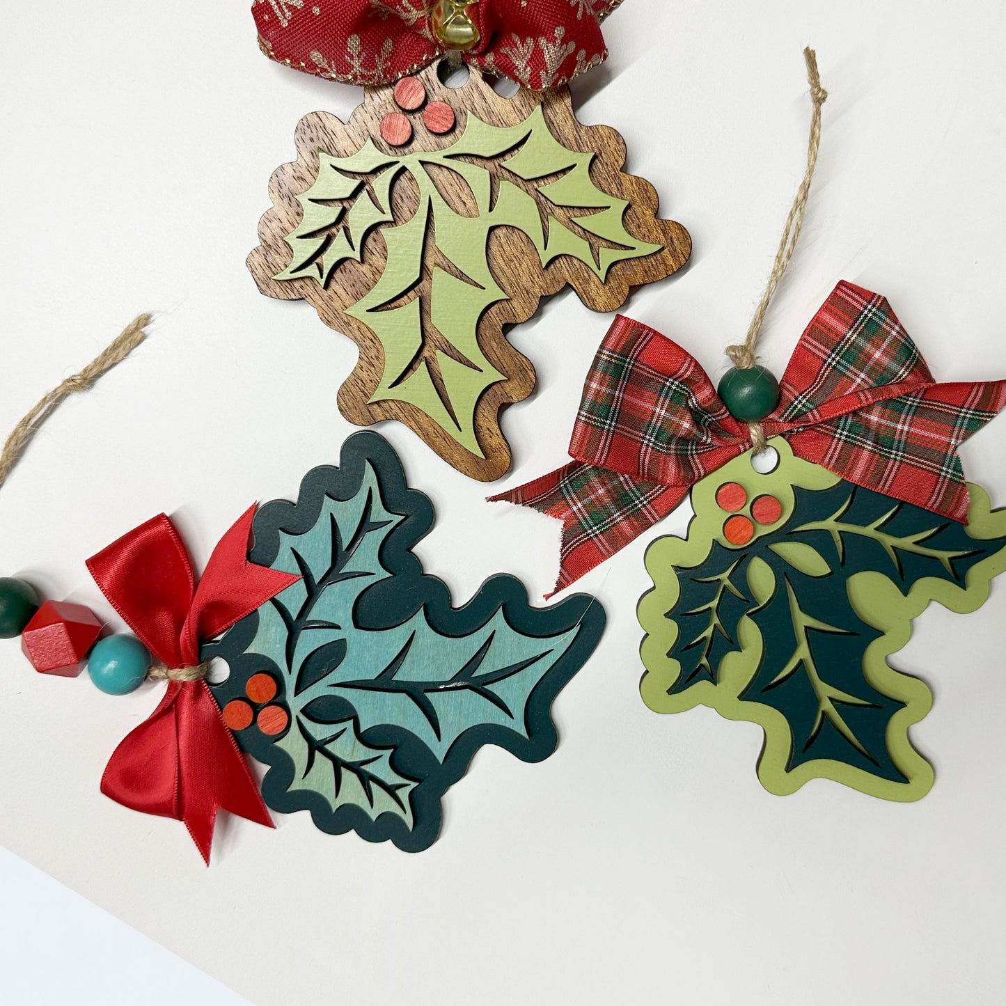 Decorative holly leaf ornaments with red bows on a white background