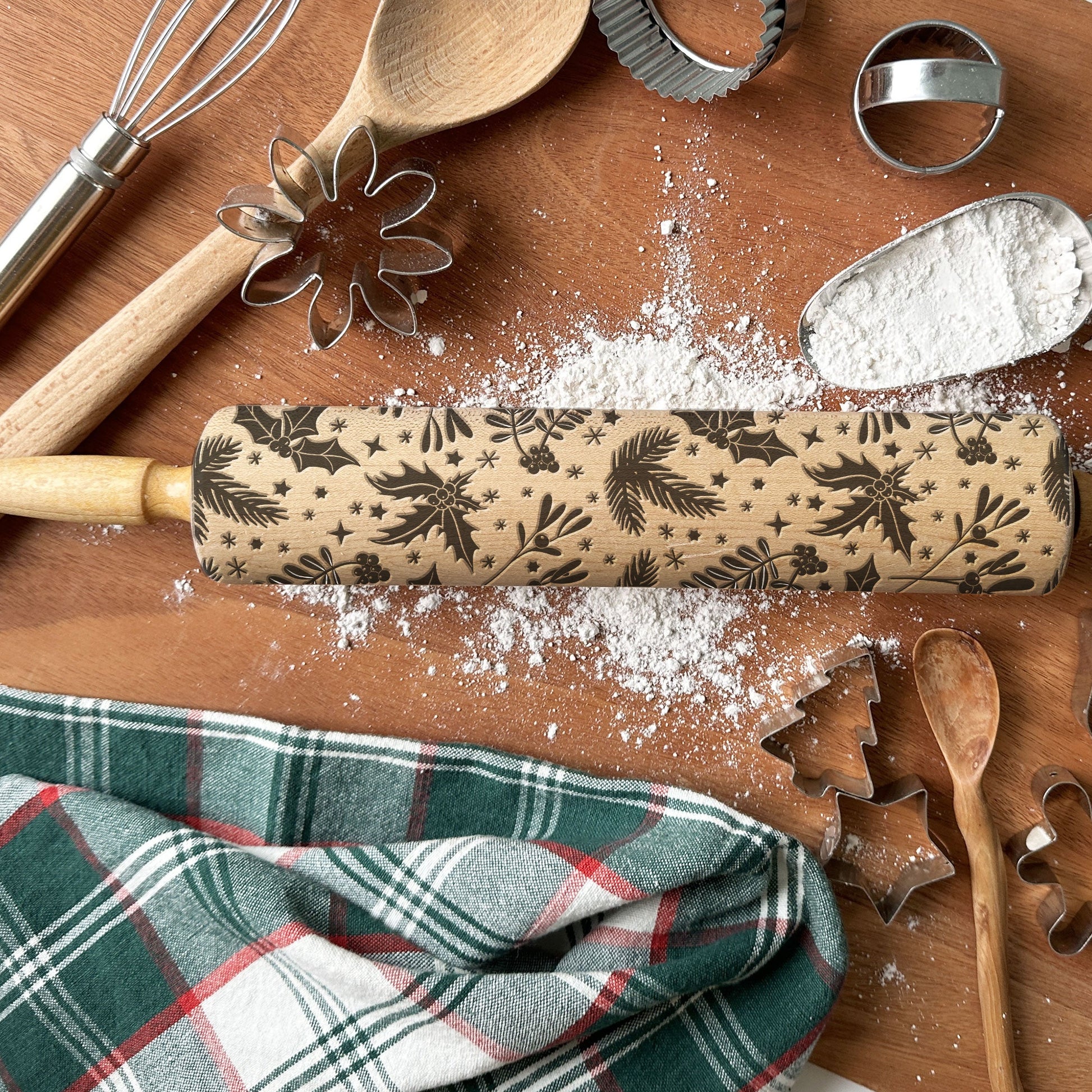 Baking tools including a rolling pin with Christmas patterns, wooden spoons, and cookie cutters on a wooden surface.