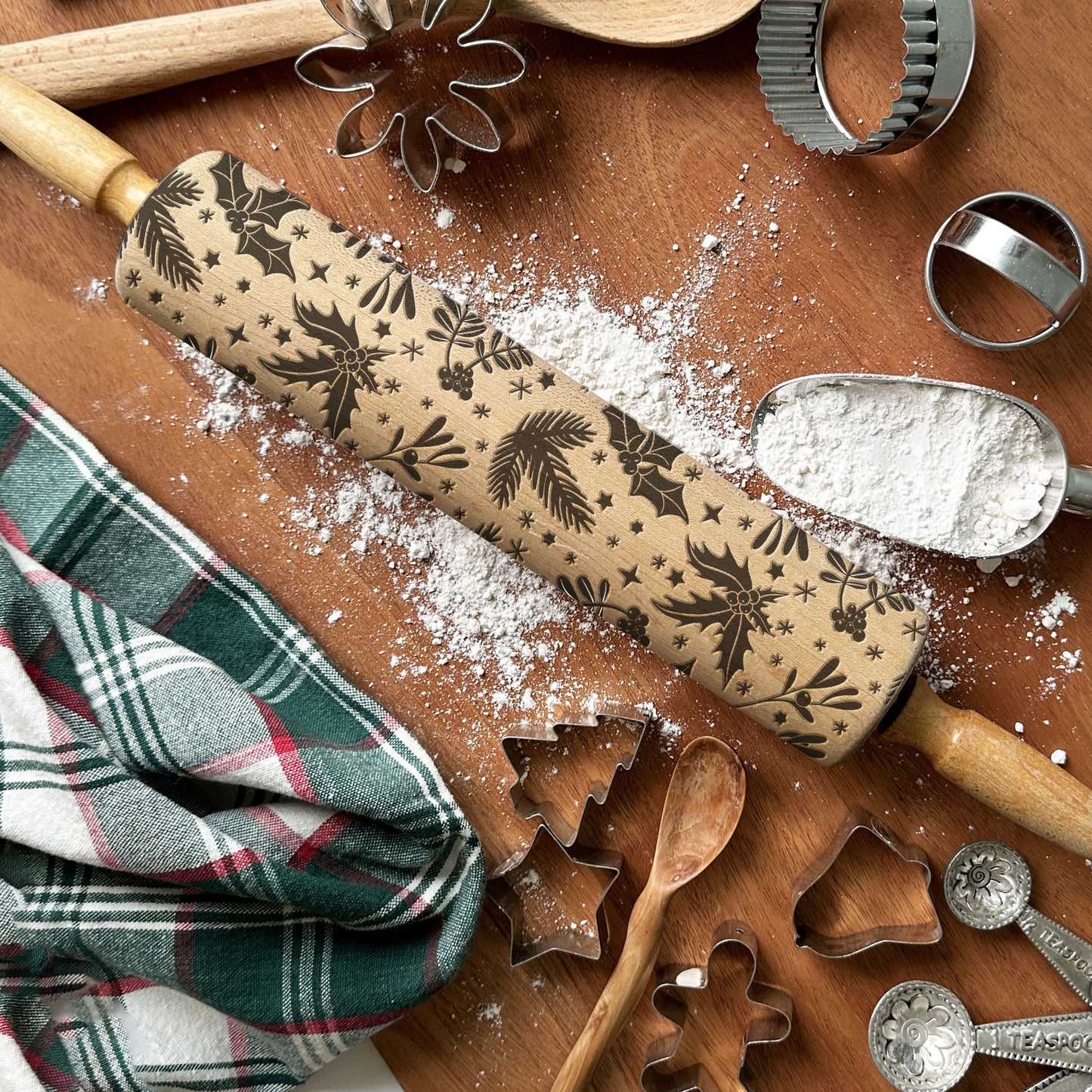 Rolling pin with Christmas patterns on a wooden surface with baking tools and flour.