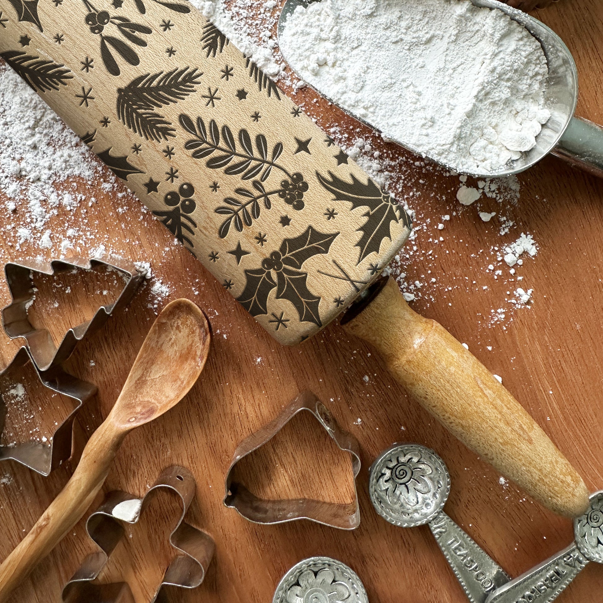 Wooden rolling pin with embossed patterns, cookie cutters, and flour on a wooden surface.