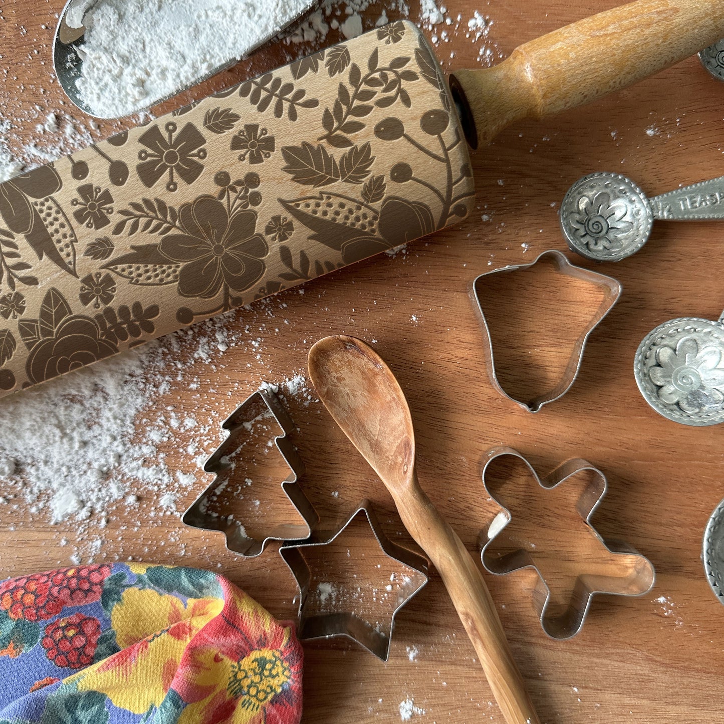 Decorative rolling pin with floral patterns on a wooden surface with cookie cutters and flour.