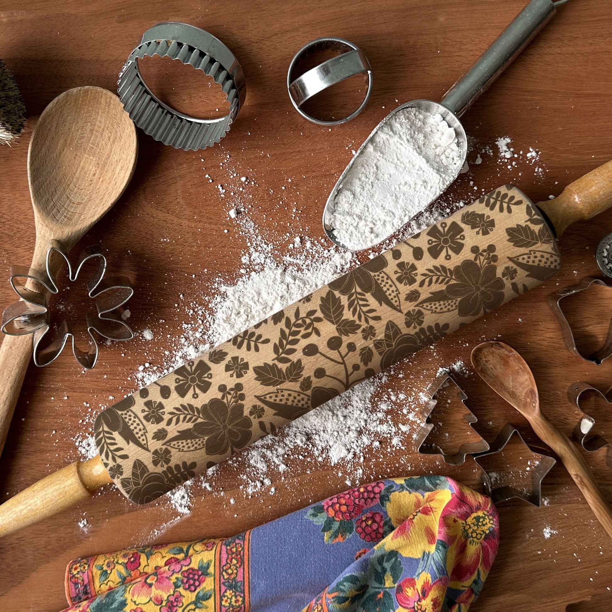 Decorative rolling pin with floral patterns on a wooden surface with flour and baking tools.