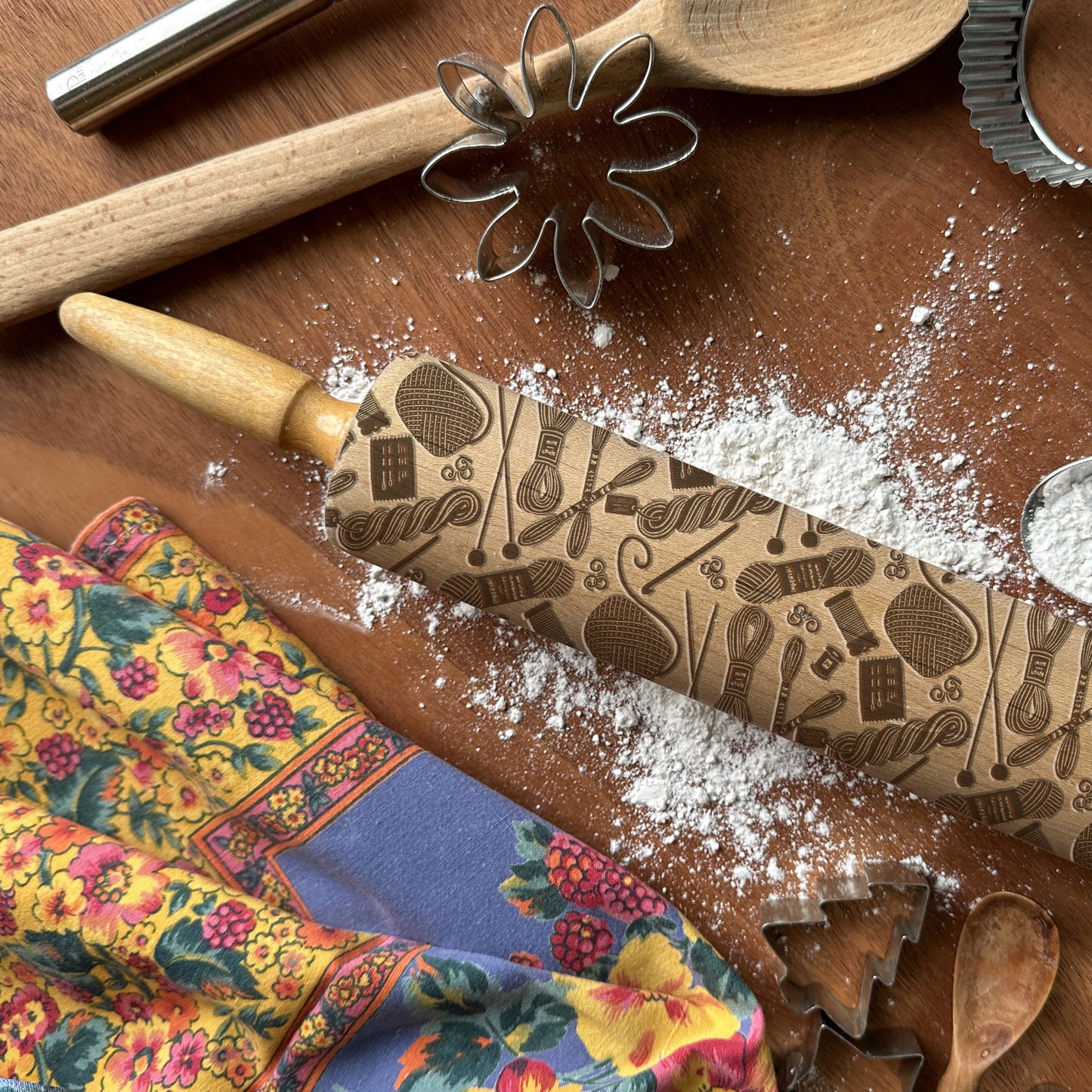 Decorative rolling pin with embossed designs on a wooden surface with flour and cookie cutters.