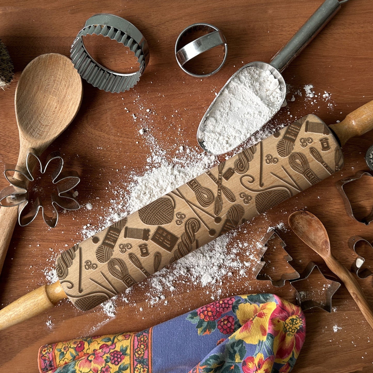 Wooden rolling pin with decorative patterns on a wooden surface with flour and kitchen tools.