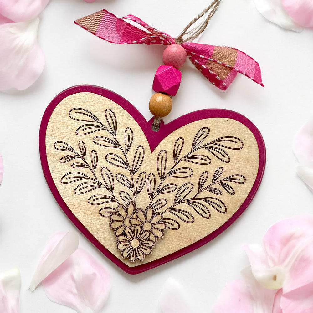 Heart-shaped wooden ornament with floral design and pink ribbon on pink flower petals
